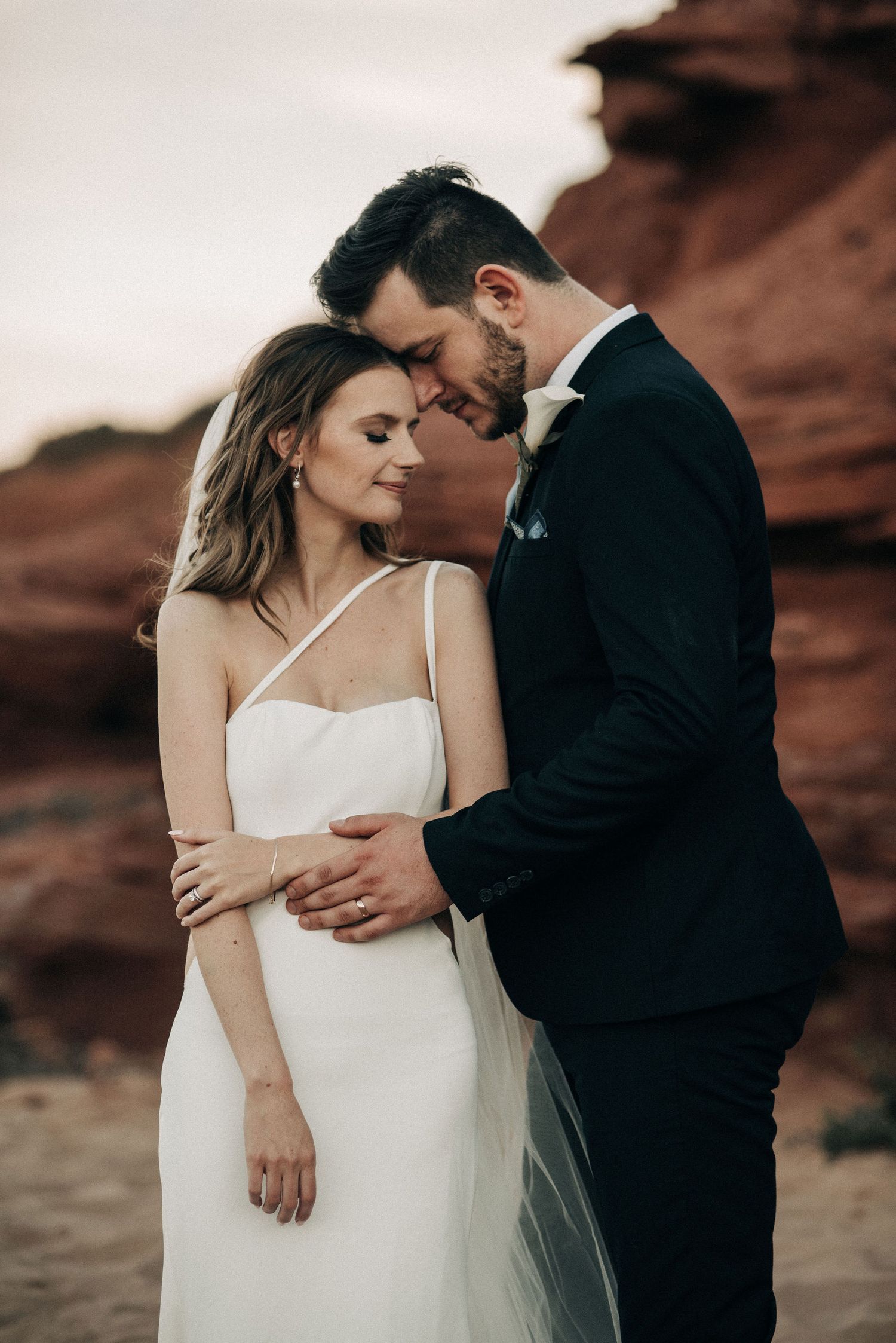 Intimate wedding couple pose against dramatic red rock formations at sunset.