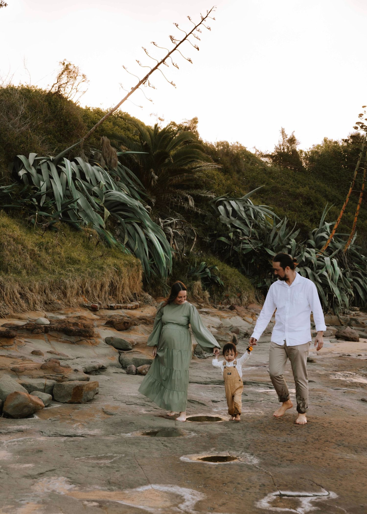 Mum, dad and their toddler sharing a peaceful moment on a beach in the sunset. Family and maternity outdoor photoshoot in Wollongong.