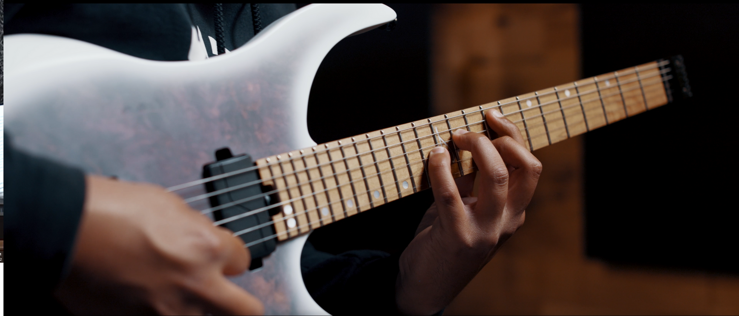 Close-up shot of hands playing a white electric guitar with wooden fretboard.