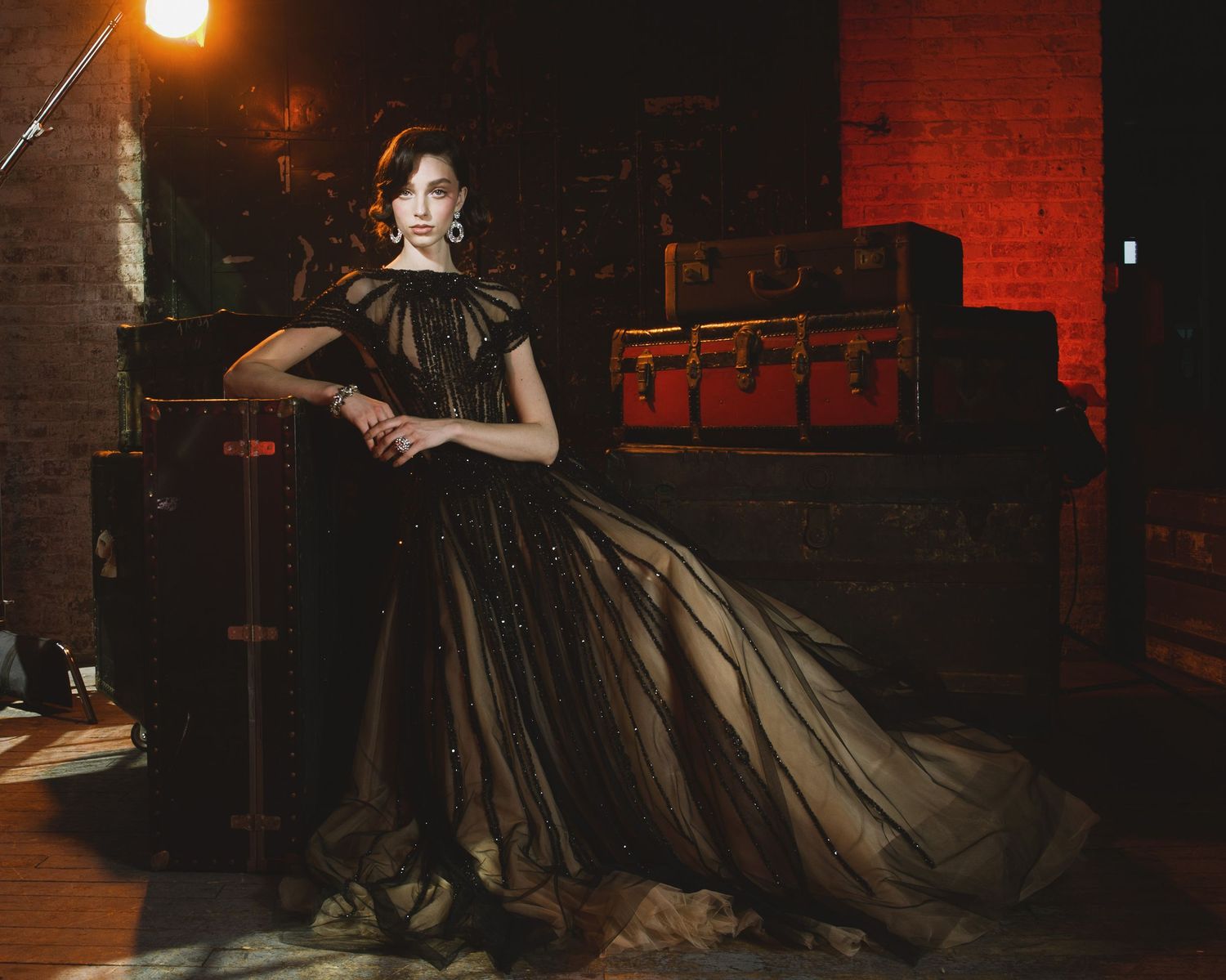 A woman in a dramatic black ball gown poses gracefully in a dimly lit vintage-style room.