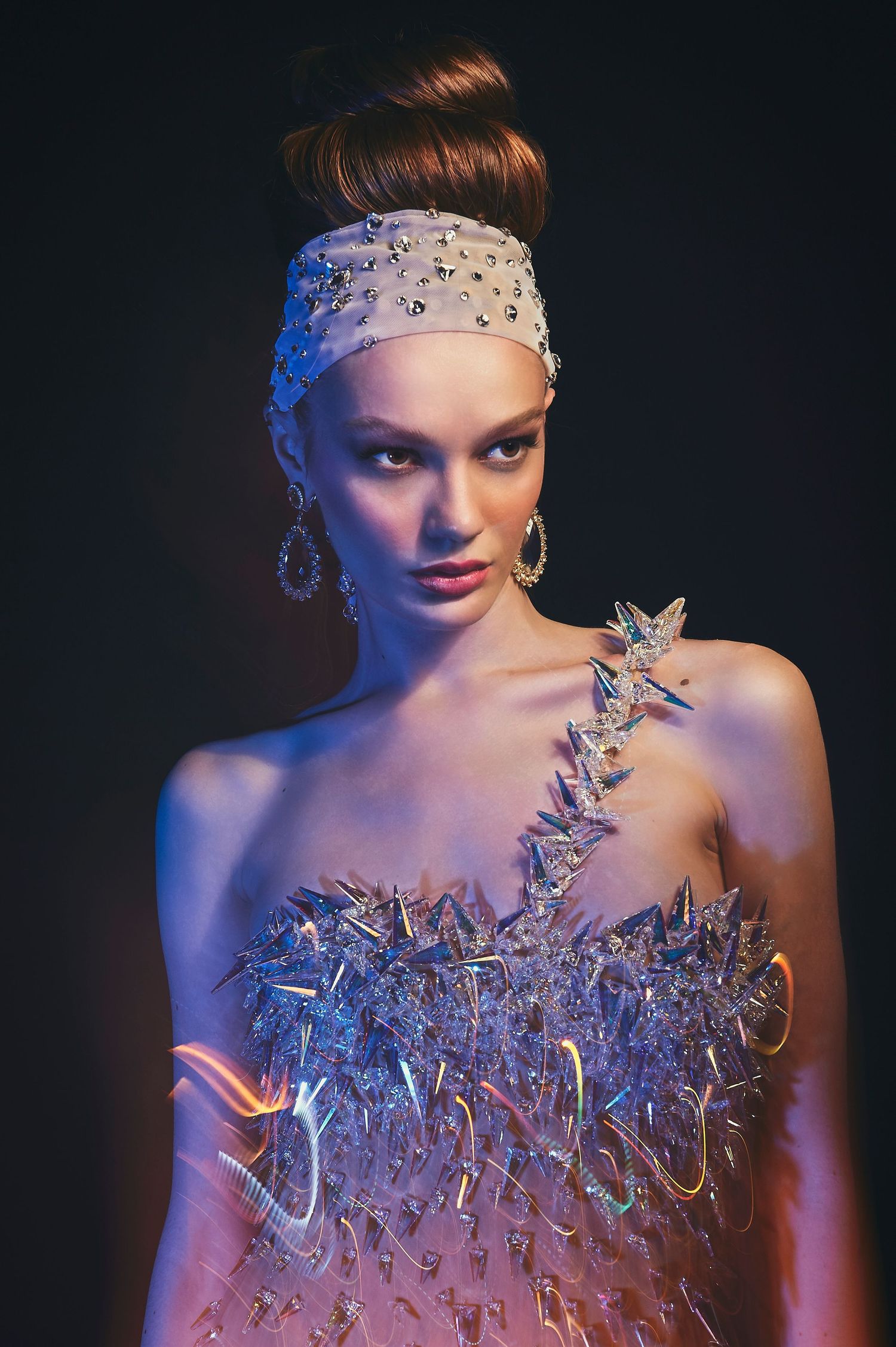 A model wears a crystal-embellished outfit with a beaded headband against a dark background.