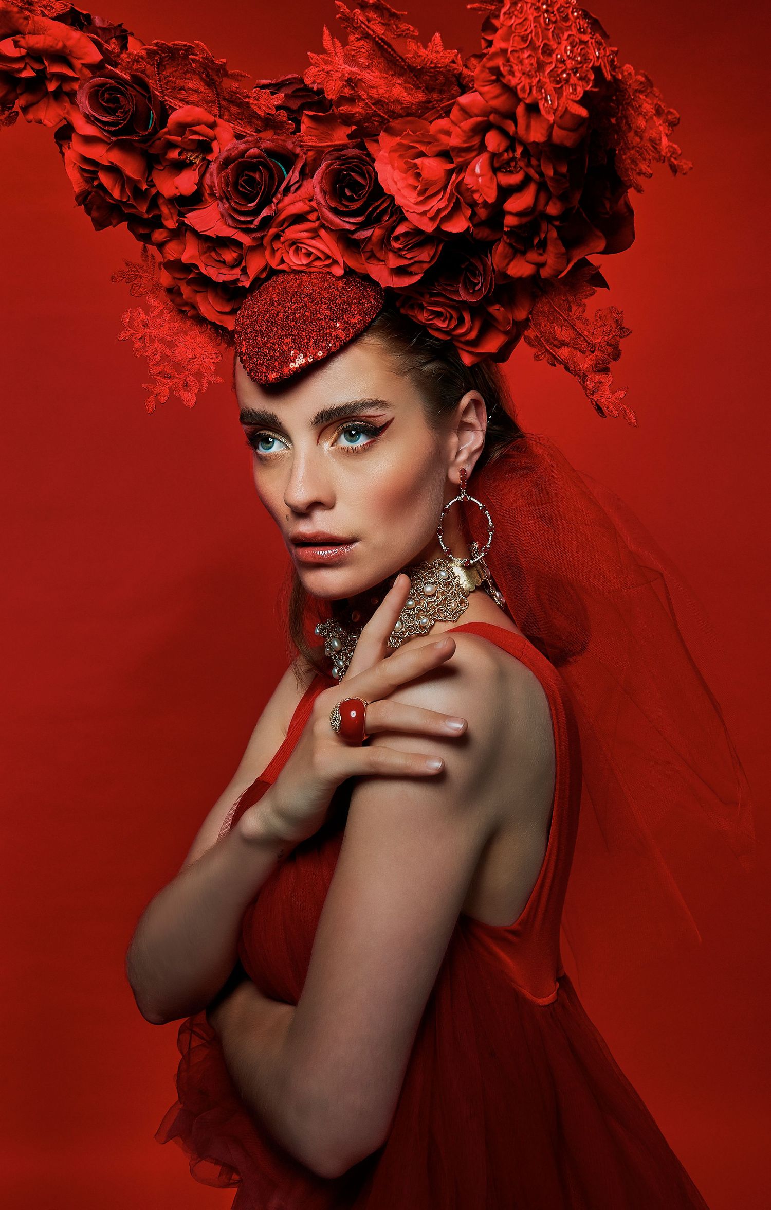 A model in a red dress wears an elaborate floral headpiece against a bold red background.