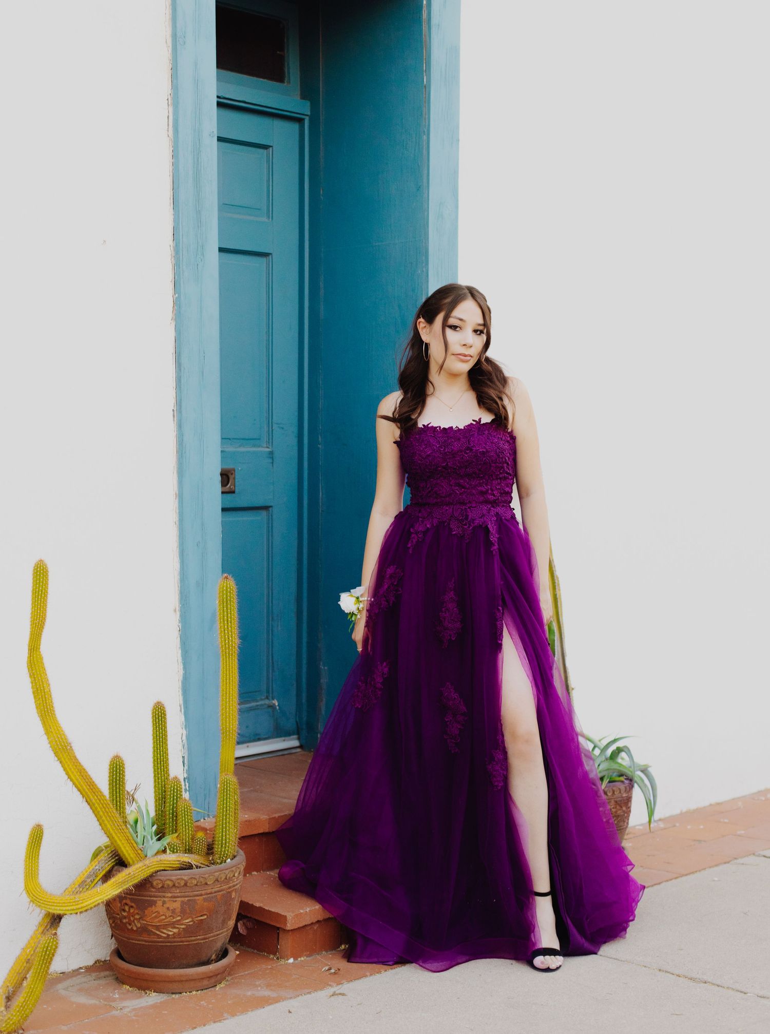 A person in a purple ball gown poses in front of a turquoise door with desert plants.