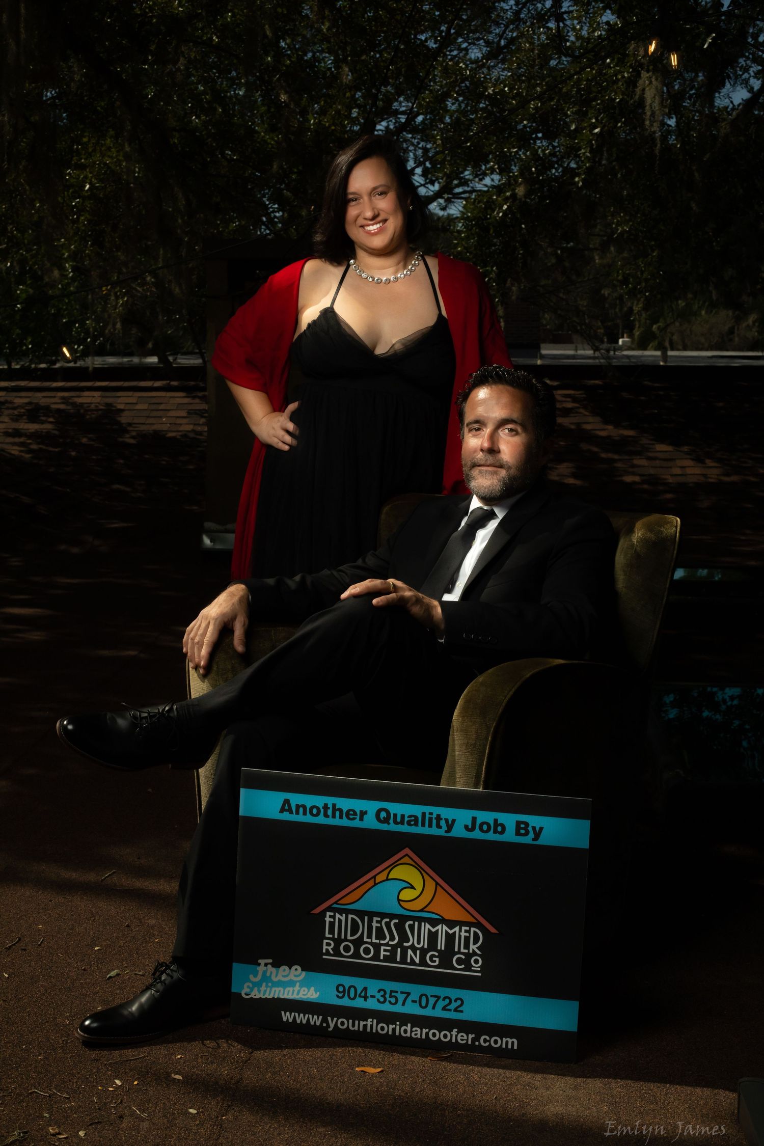 A formal portrait photoshoot featuring a couple in elegant black attire with promotional signage.