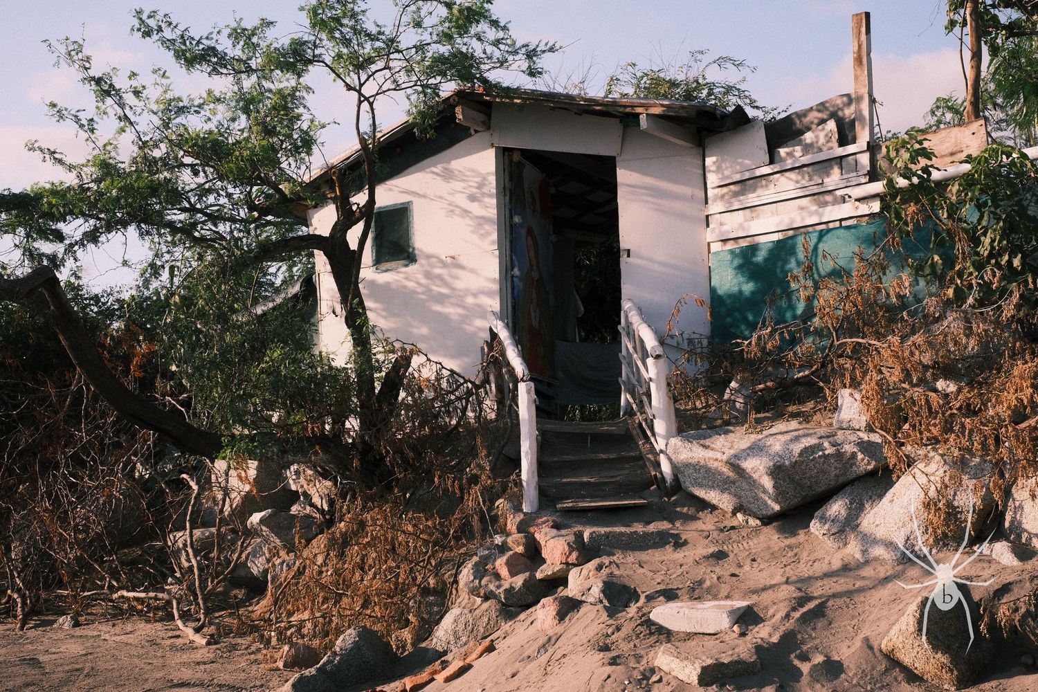 Small white building with steps on rocky terrain under bright sunlight.