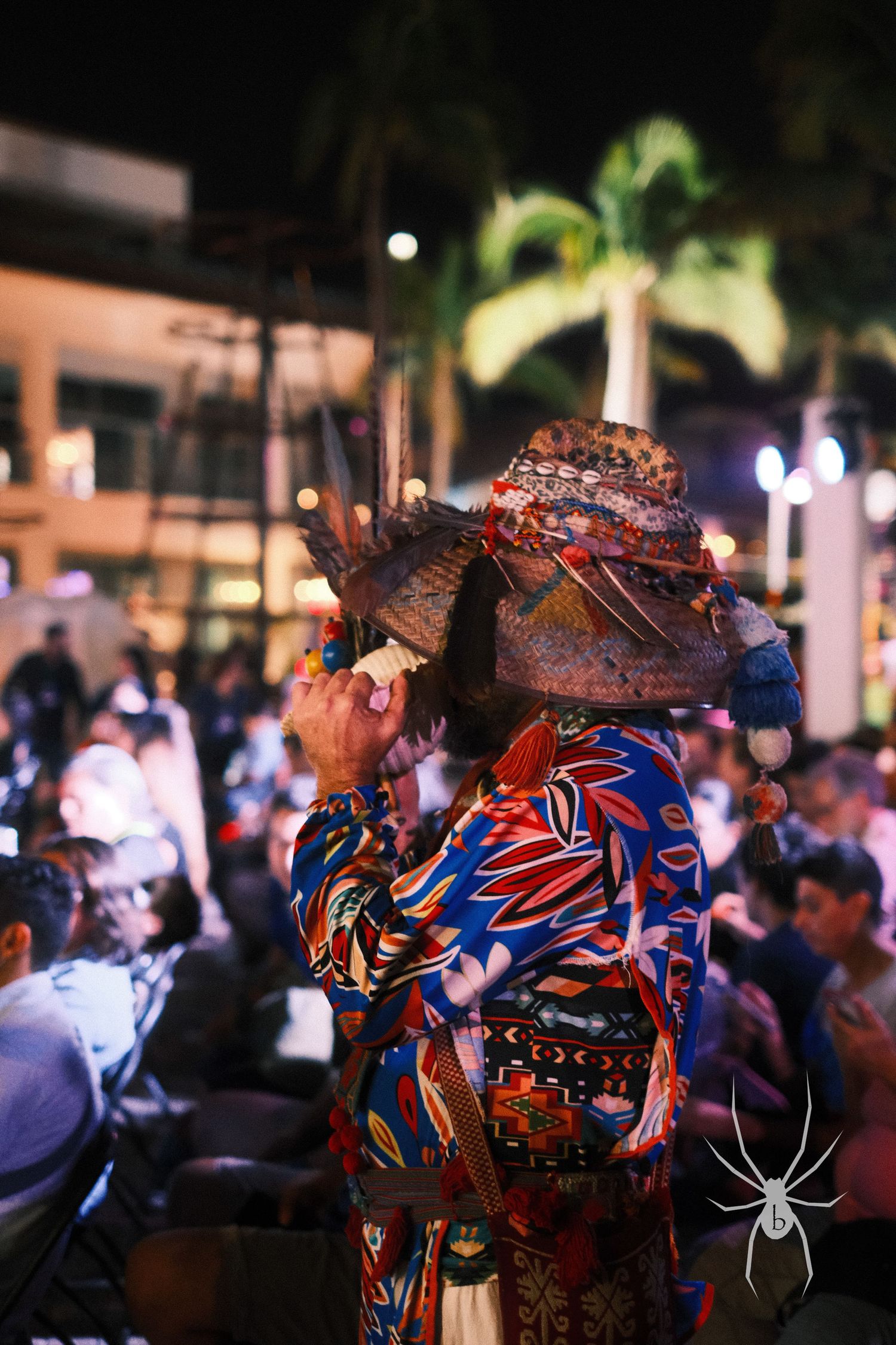 Person in colorful traditional Mexican attire attending a Dia de los Muertos celebration at night.