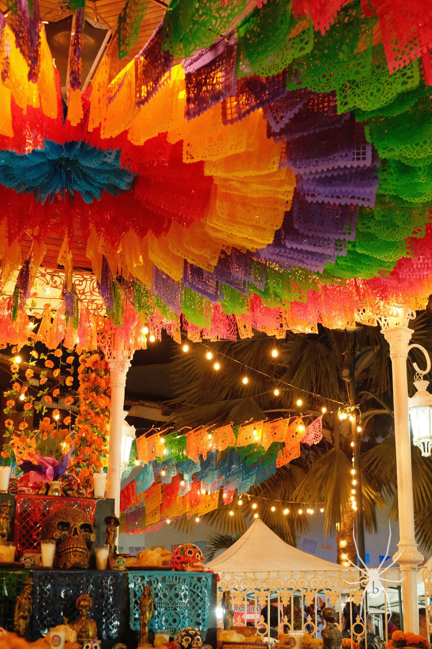 Vibrant papel picado banners in rainbow colors hanging with string lights at a Mexican festival.