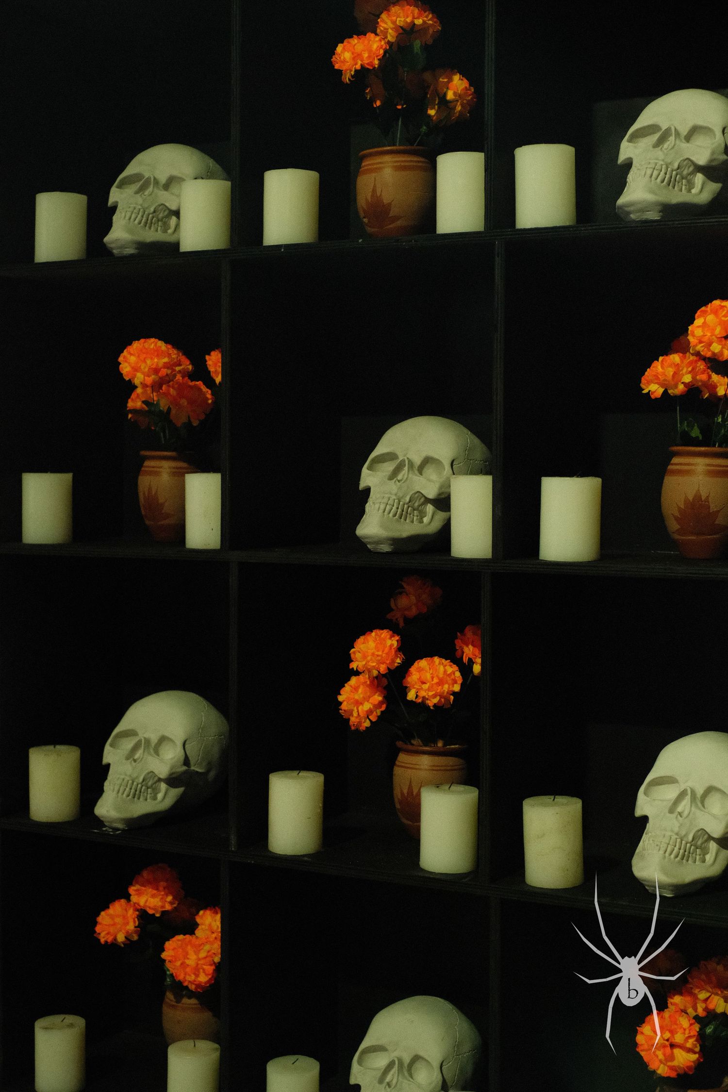 Dark display of skulls and white candles arranged with orange marigolds on black shelving.