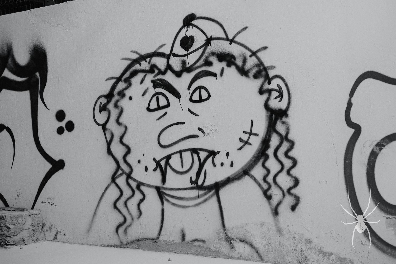 A black and white graffiti art depicting a quirky cartoon character with curly hair and exaggerated features on a wall.