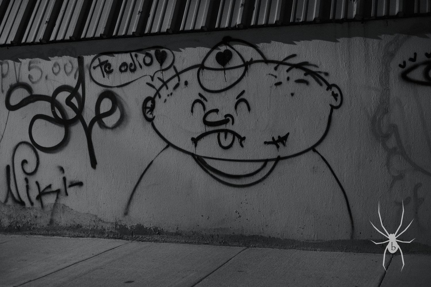 Black and white street art showing a simple cartoon face with one eye and tongue sticking out.