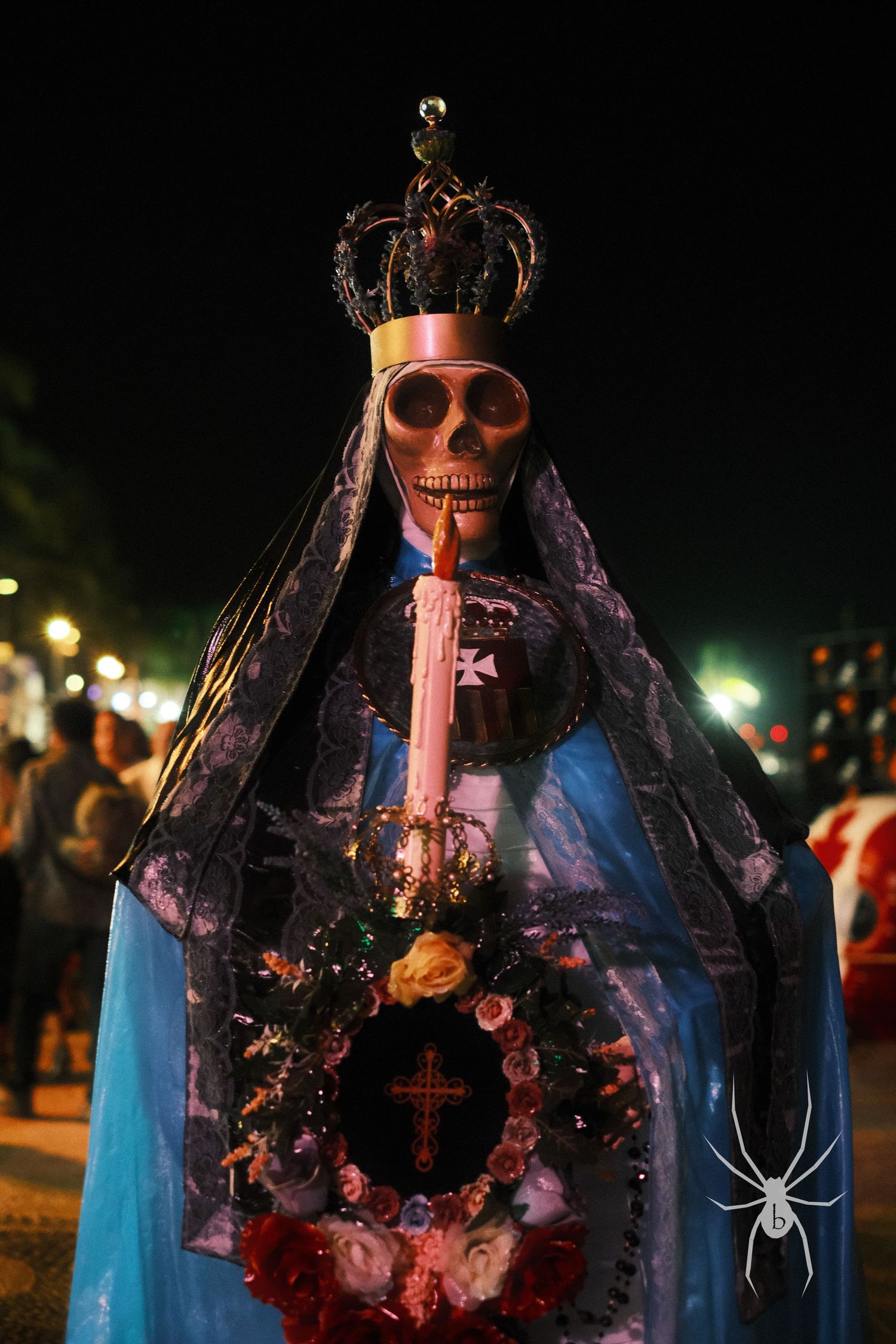 Decorated skeleton figure wearing a crown and blue robes displayed at night festival.