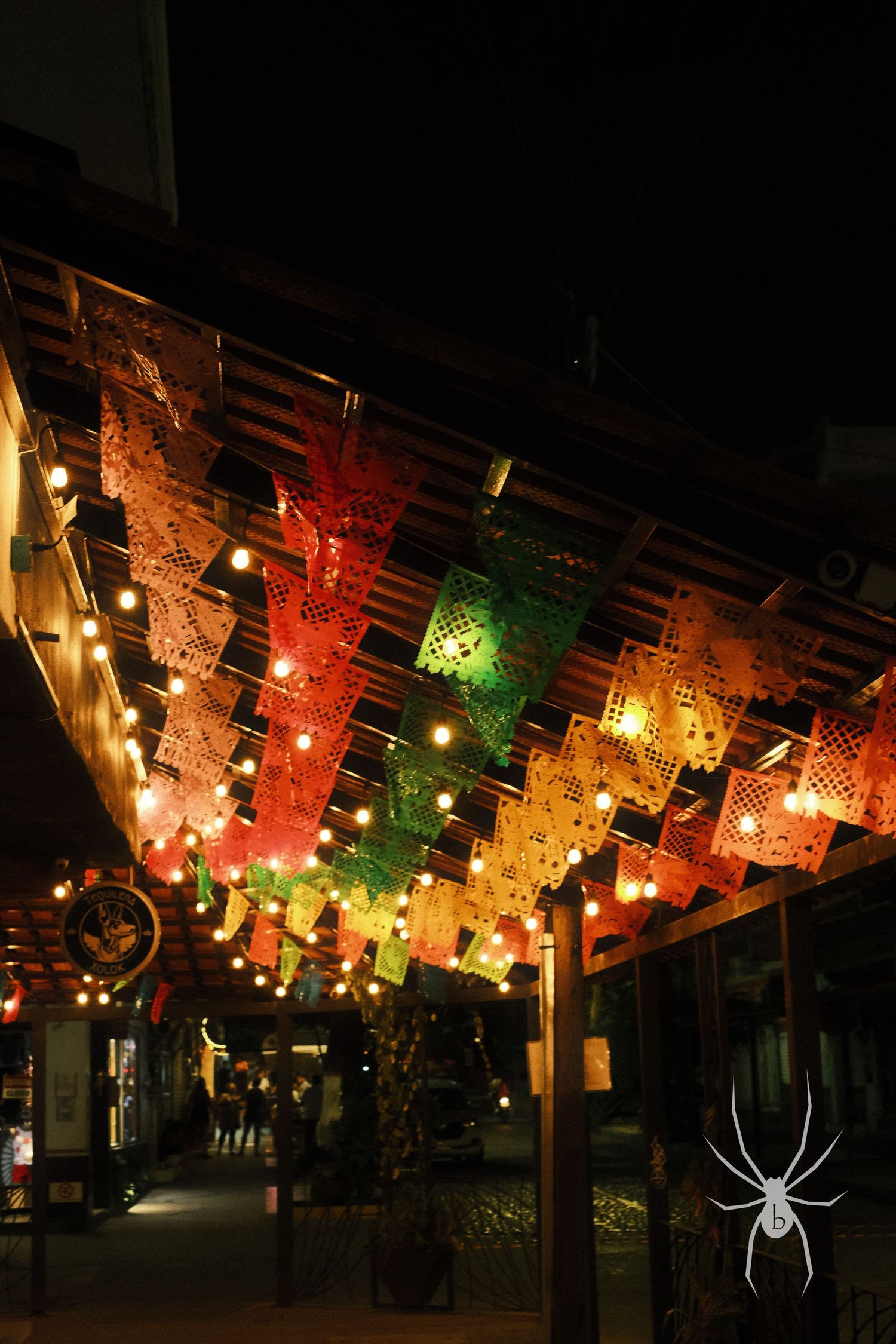 Colorful paper lanterns and string lights create a festive canopy overhead at night.