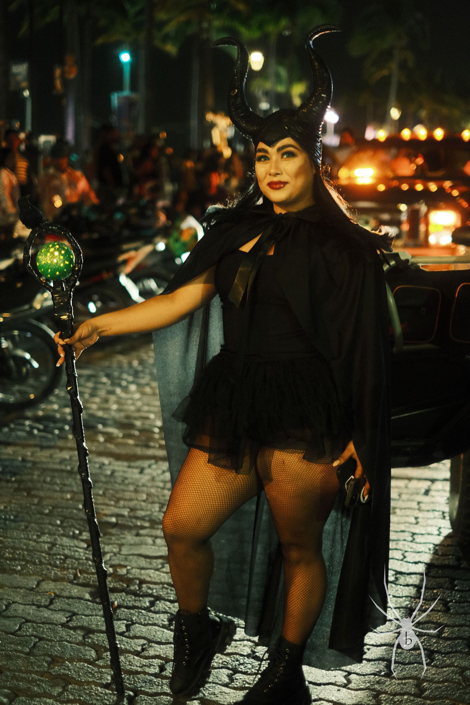 Halloween costume featuring horned headpiece and black cape on cobblestone street at night.