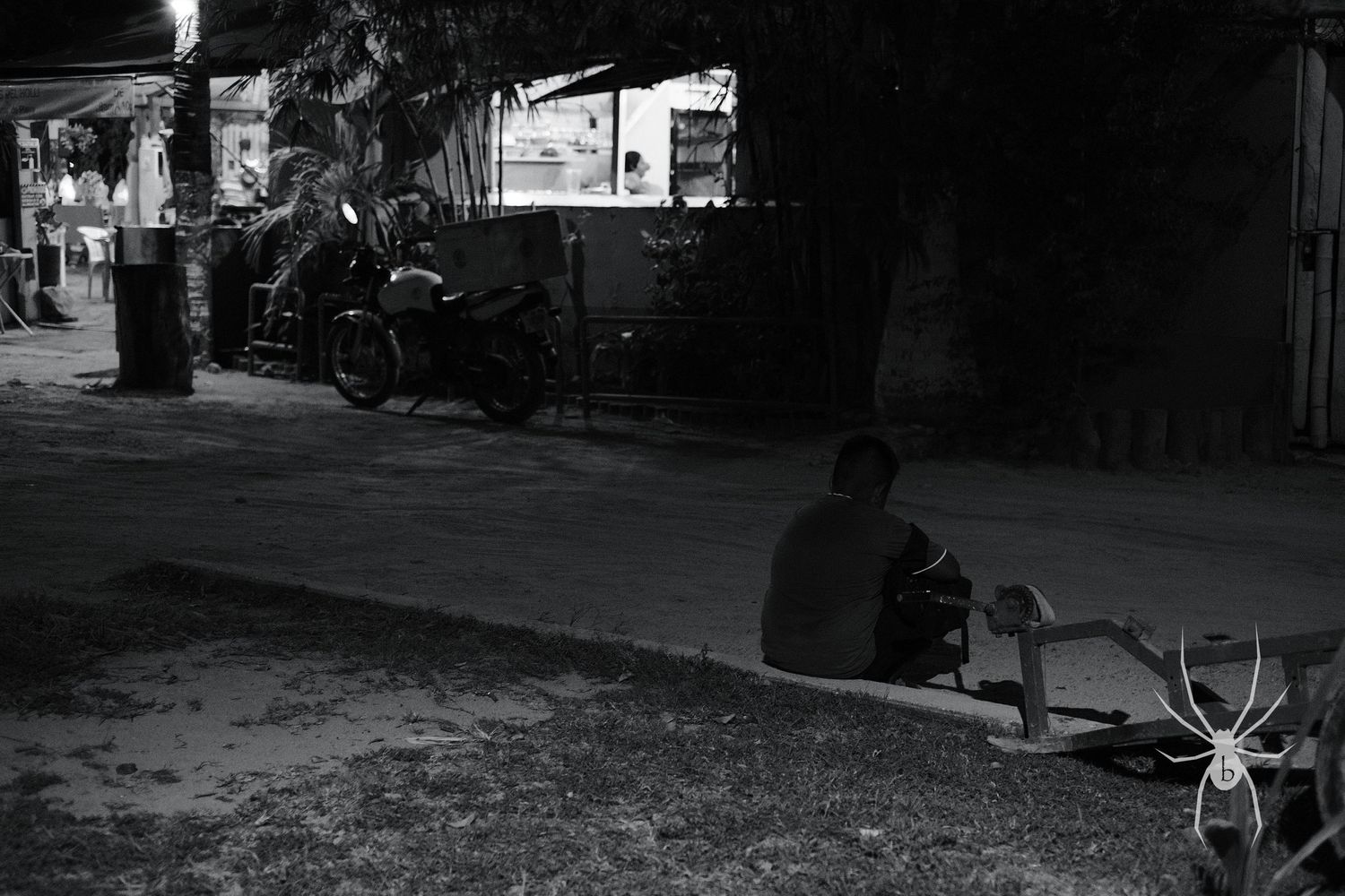 Black and white nighttime street scene with a silhouette sitting on the ground.