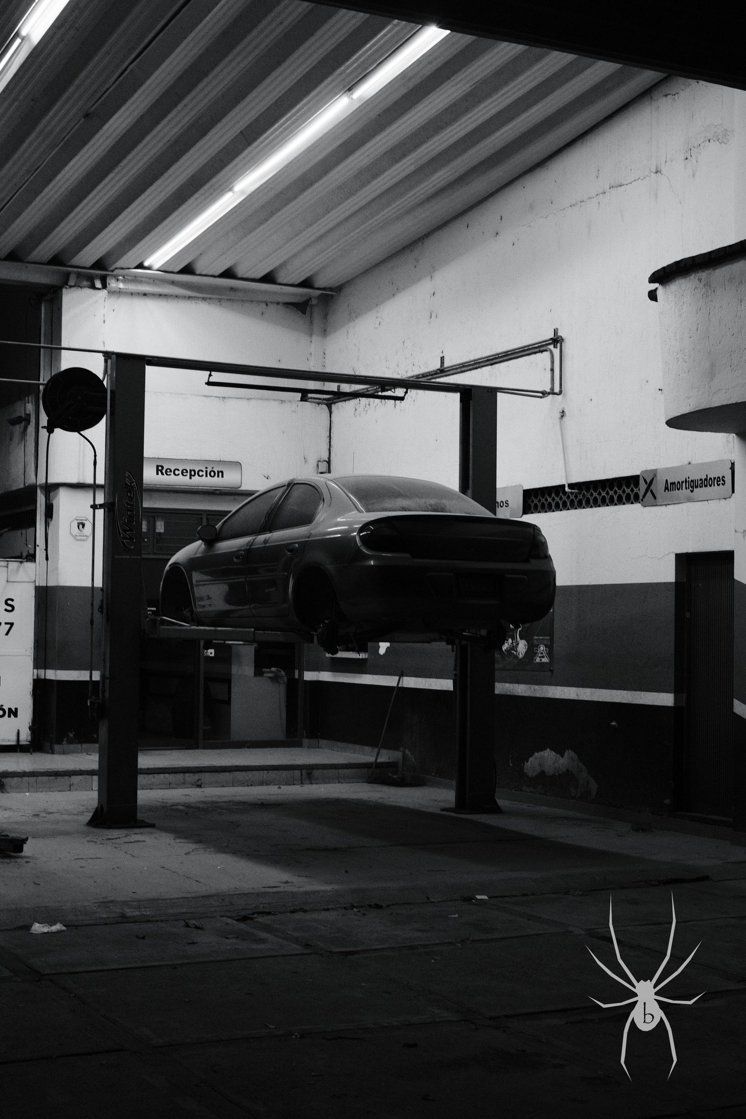 Car lifted on hydraulic lift in dimly lit auto repair garage with industrial atmosphere.