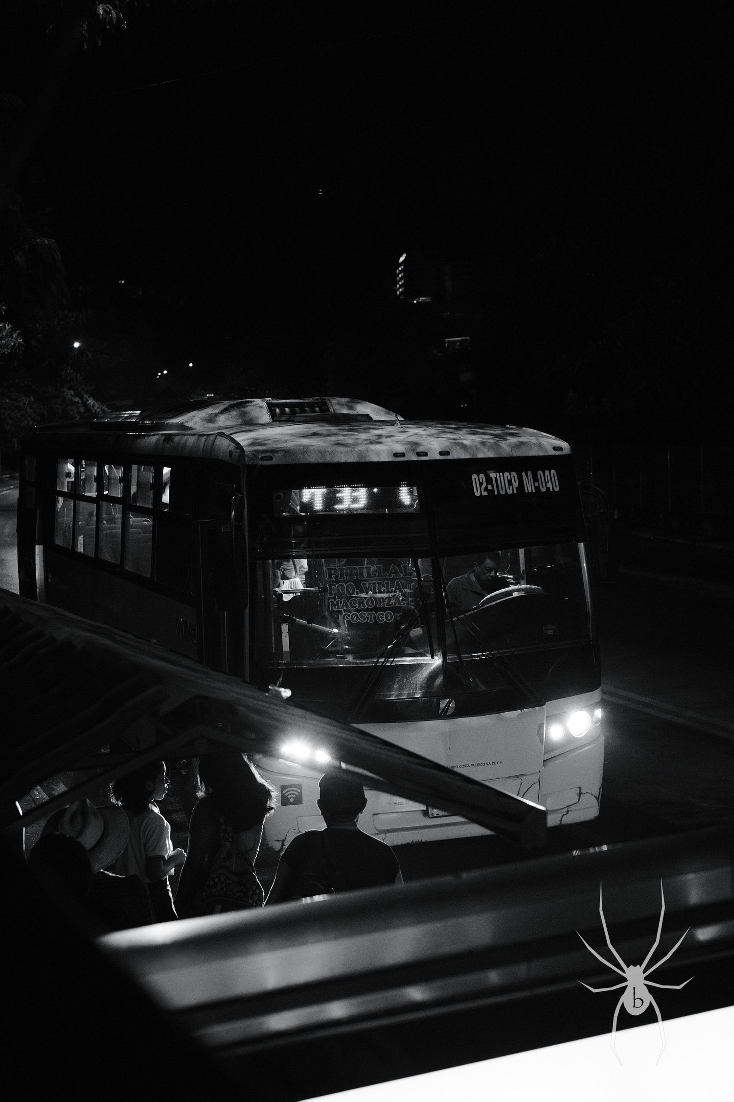 Public bus illuminated at night with silhouettes of waiting passengers.