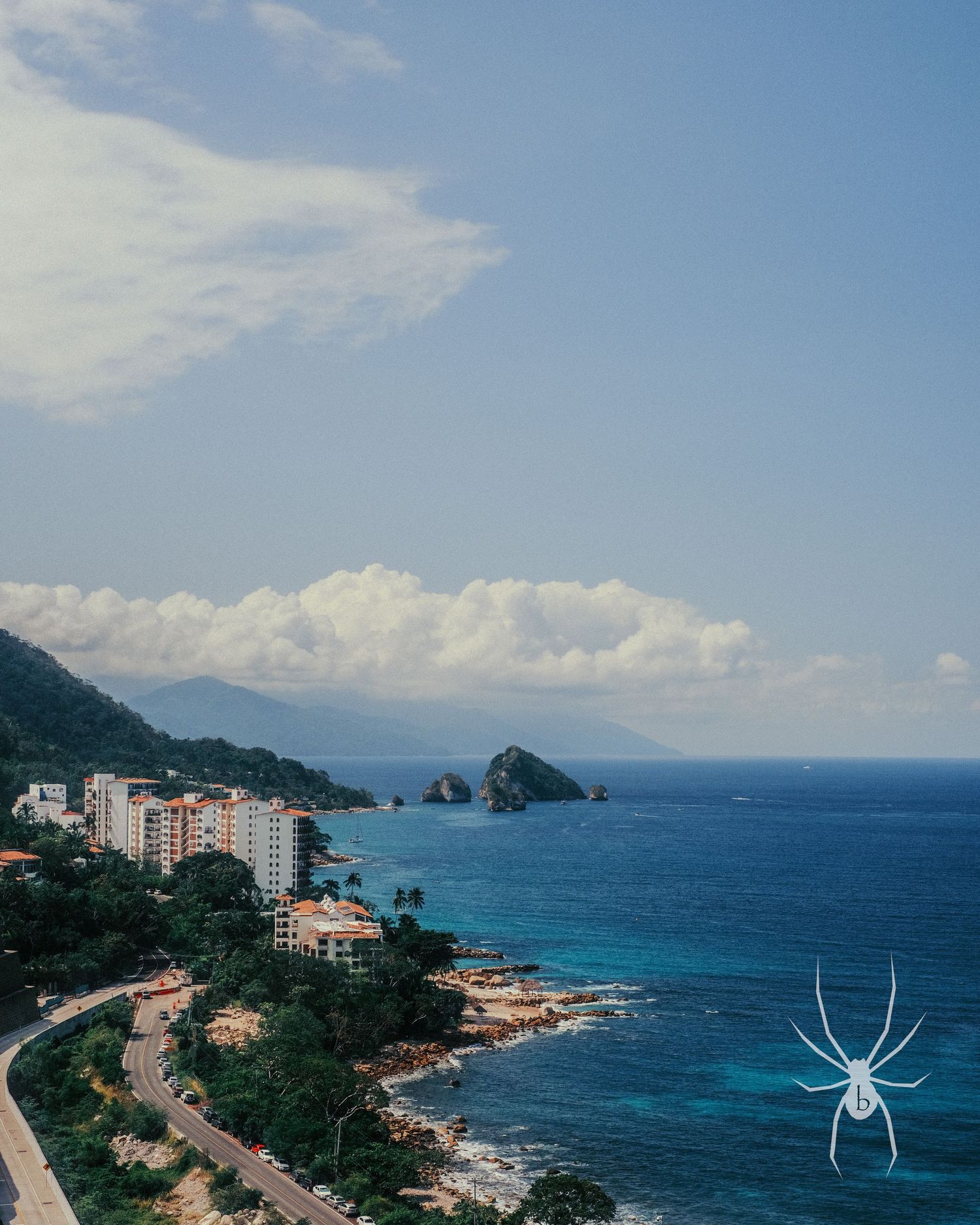 Coastal cityscape with blue ocean, mountains, and residential buildings along the shoreline.
