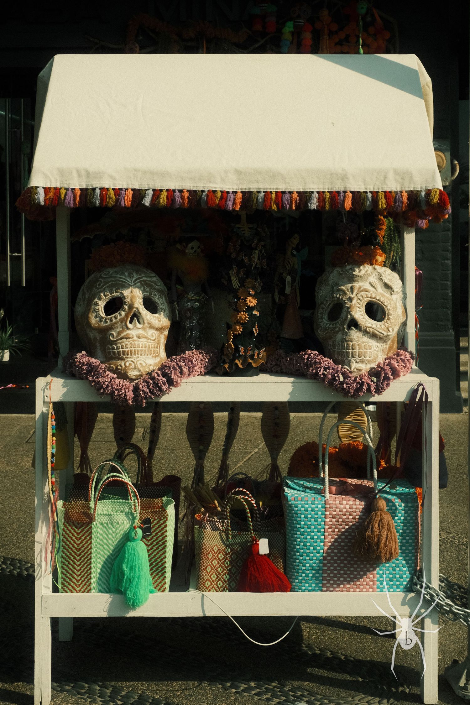 Display stand with decorative sugar skulls and colorful tasseled bags for sale.