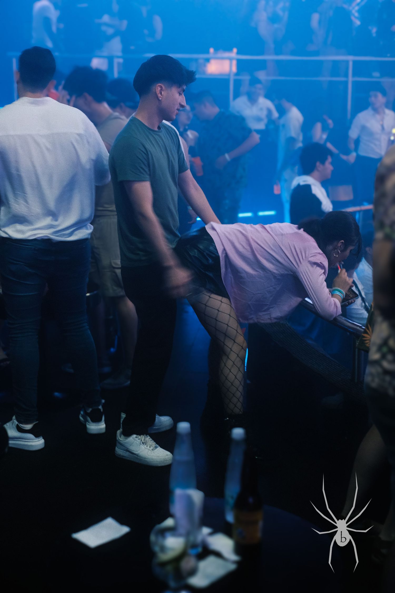 People dancing in a dimly lit nightclub with blue atmospheric lighting and fog effects.