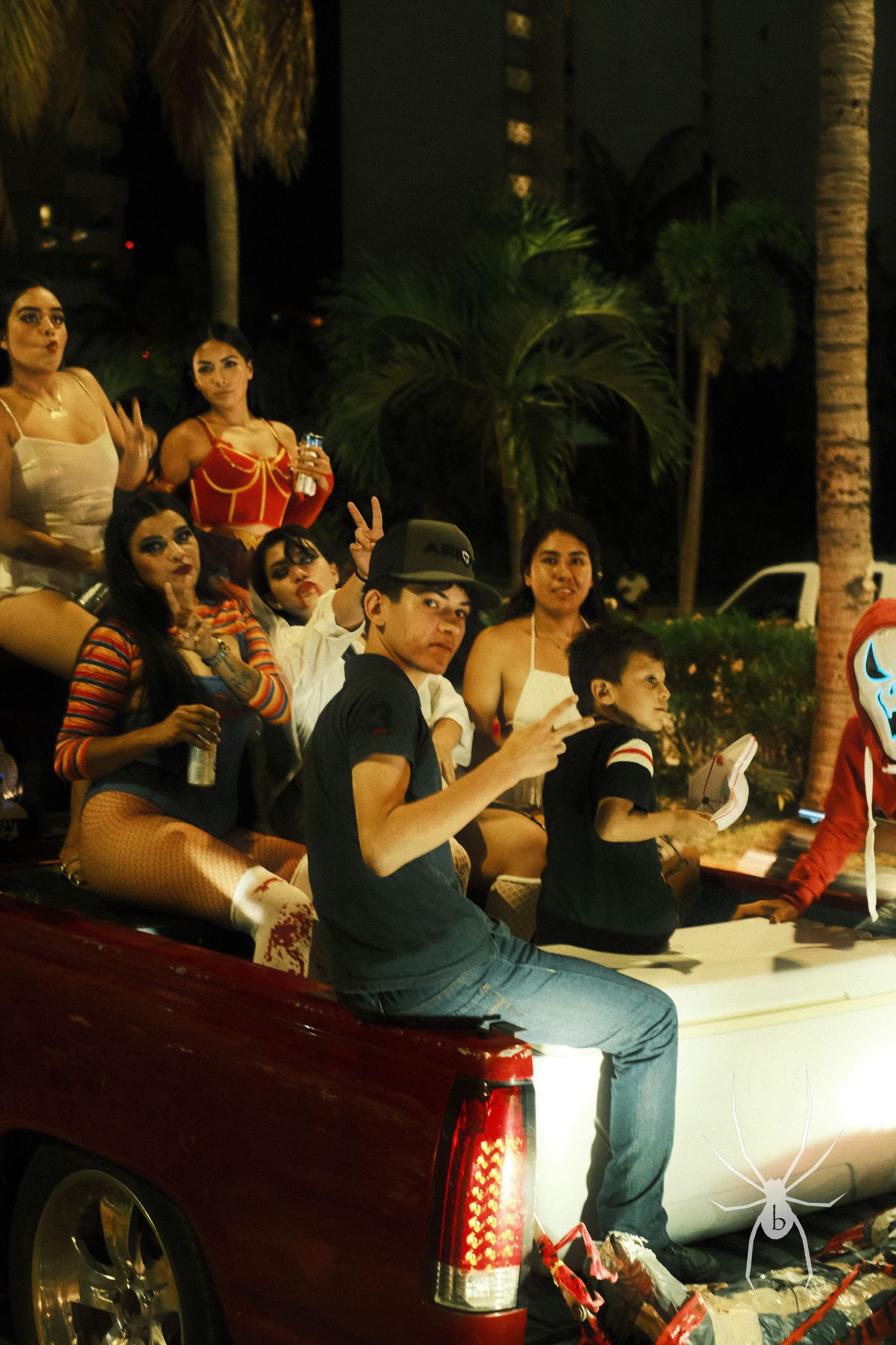 Group gathered on back of pickup truck during nighttime celebration with palm trees visible.