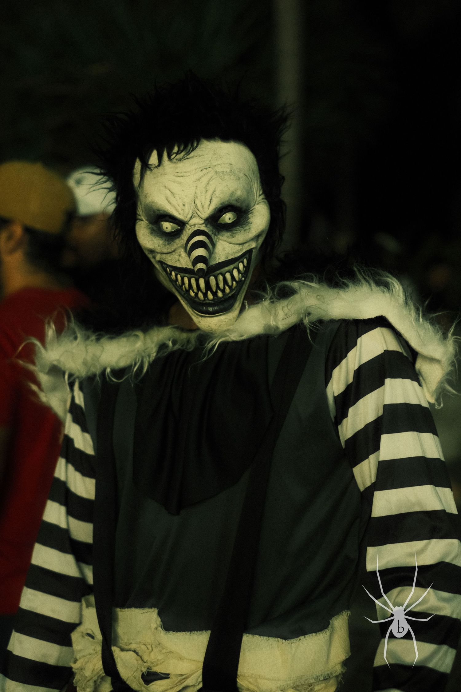 Spooky Halloween figure in striped sleeves wearing creepy monster mask poses in dark setting.