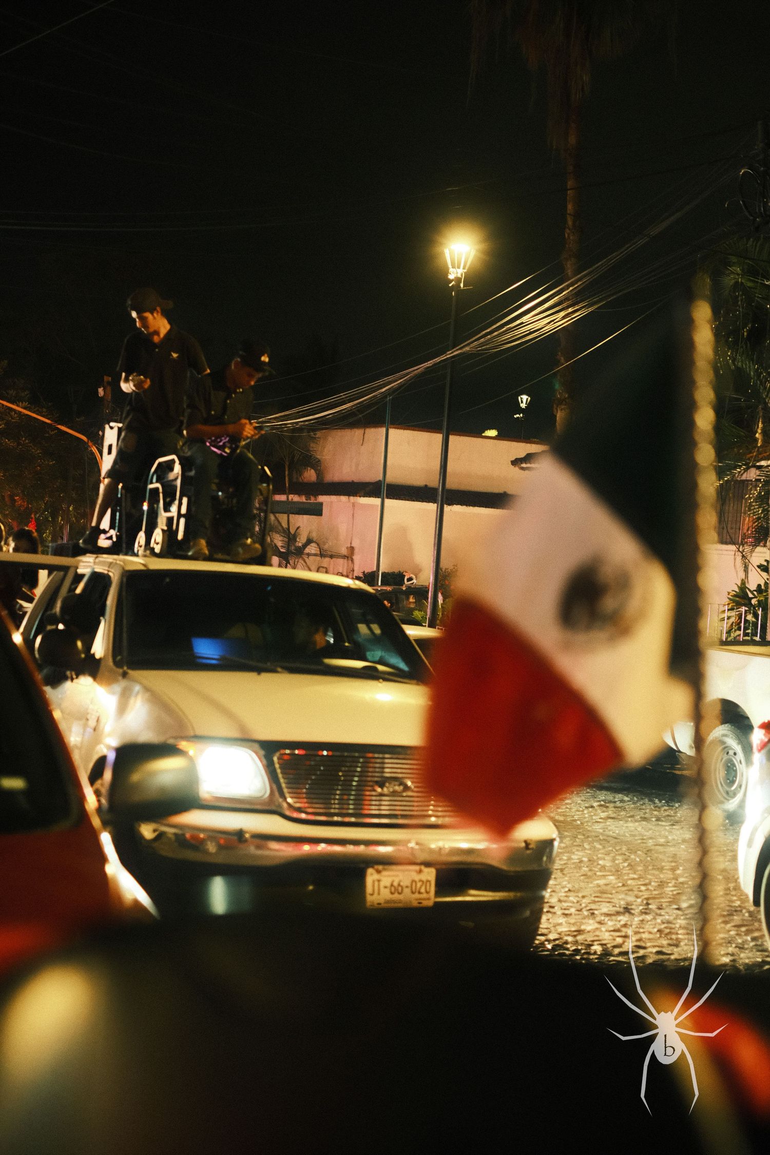 Mexican flag and car lit by streetlamp at night during a celebration.