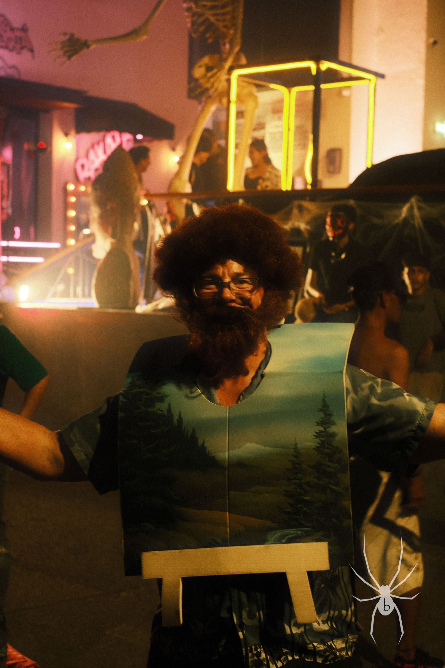 Artist painting at easel during nighttime street performance with glowing lights.