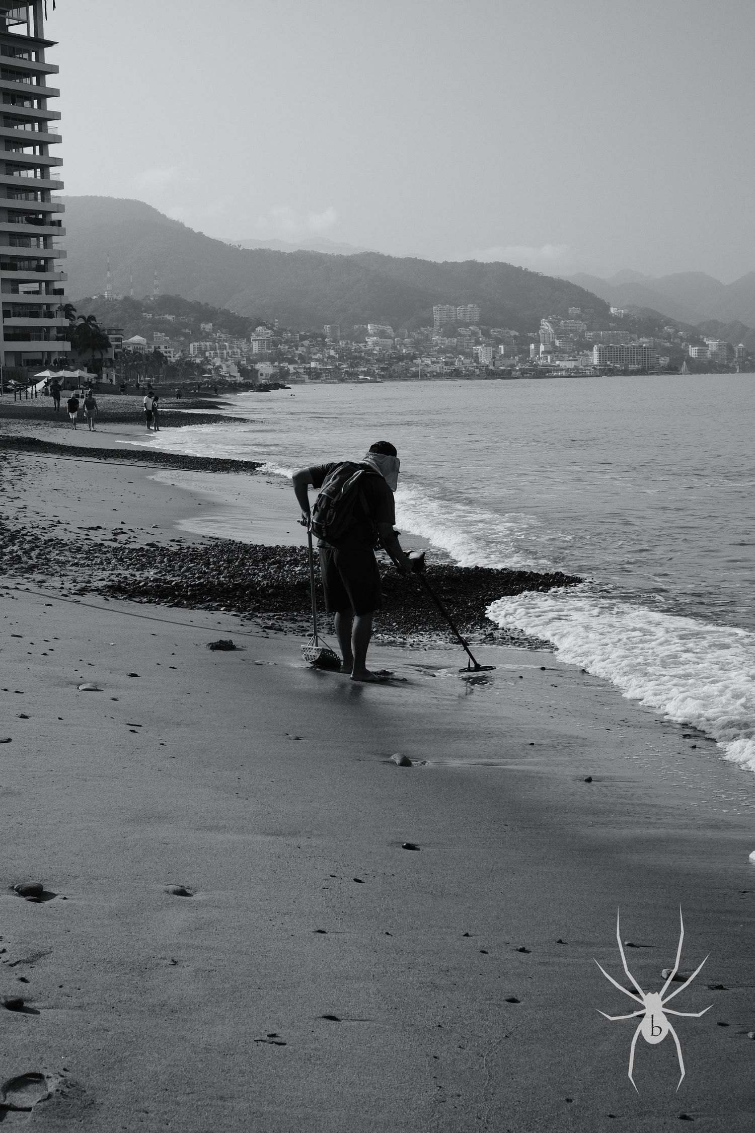 Silhouette of beachcomber searching along shoreline with mountains in background.