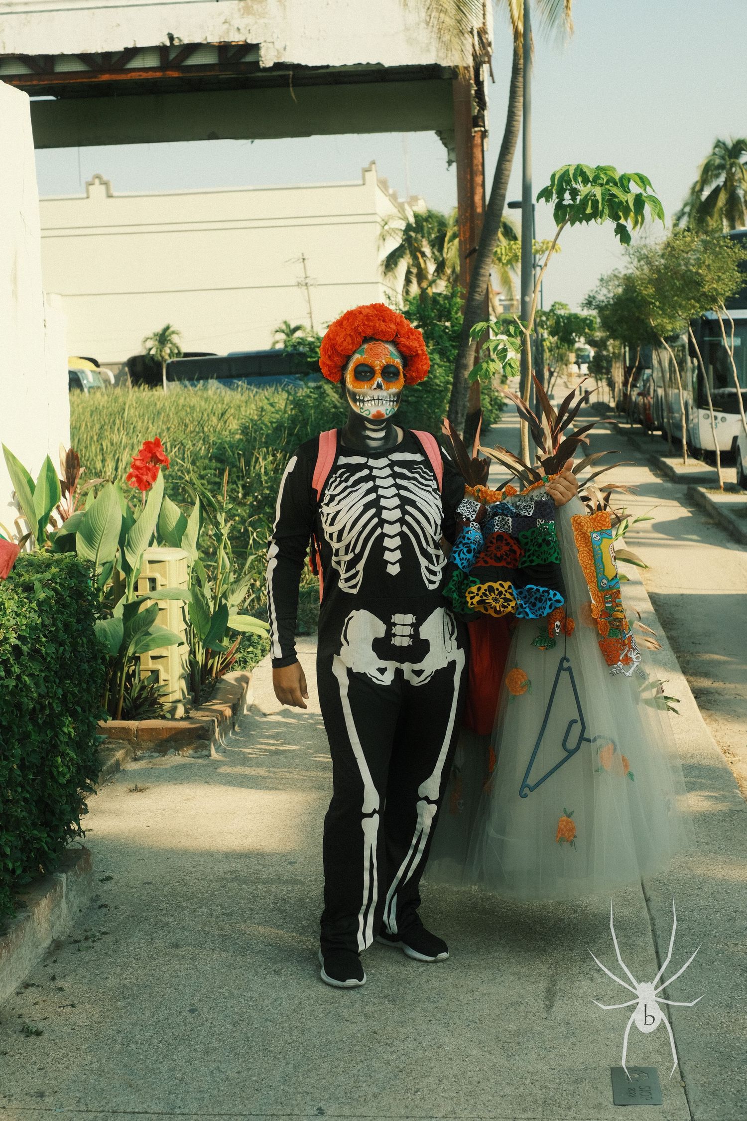 Person in skeleton costume with orange wig standing next to potted plants.