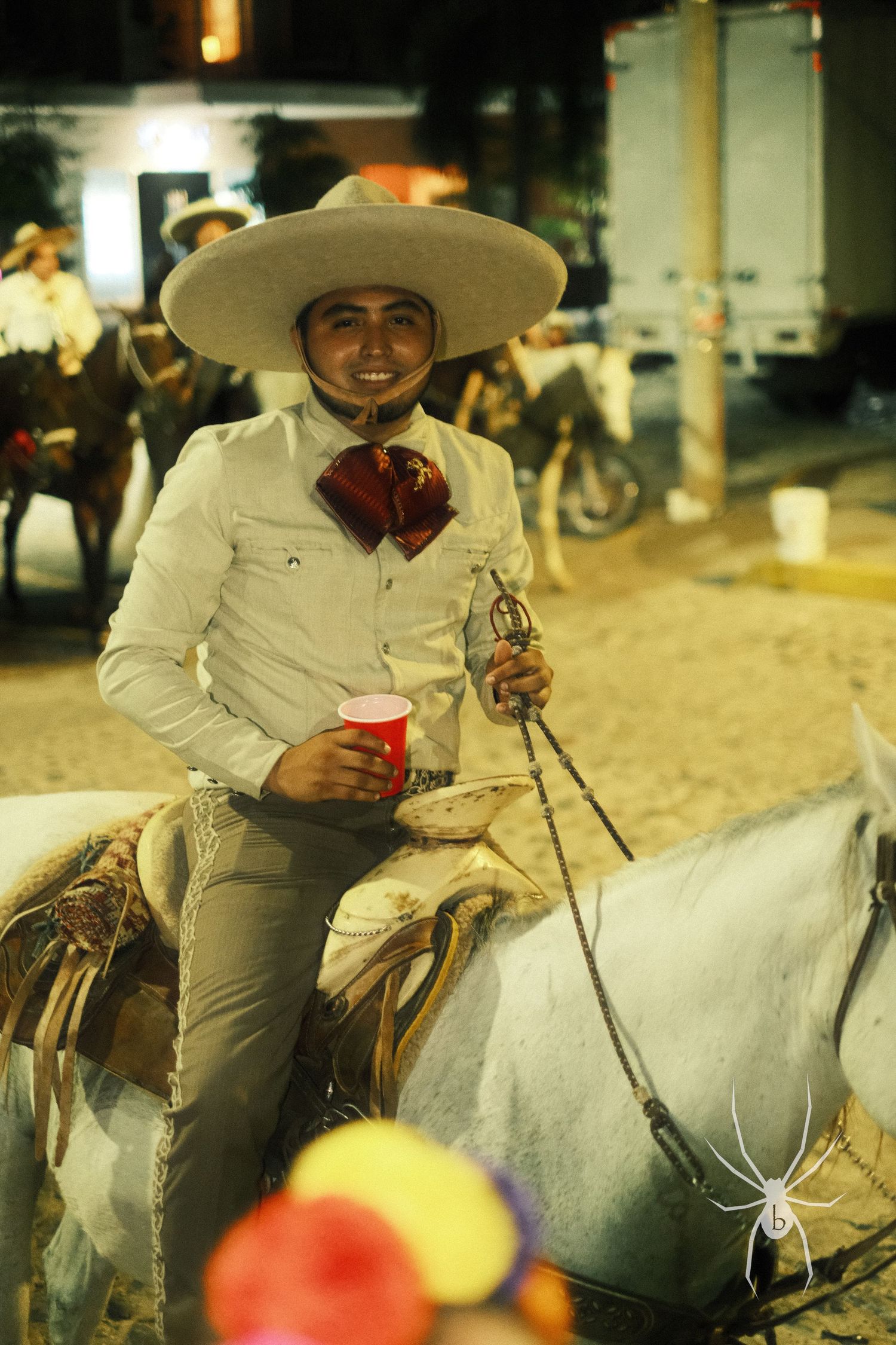 Rider in traditional Mexican attire atop a white horse during evening festivities.