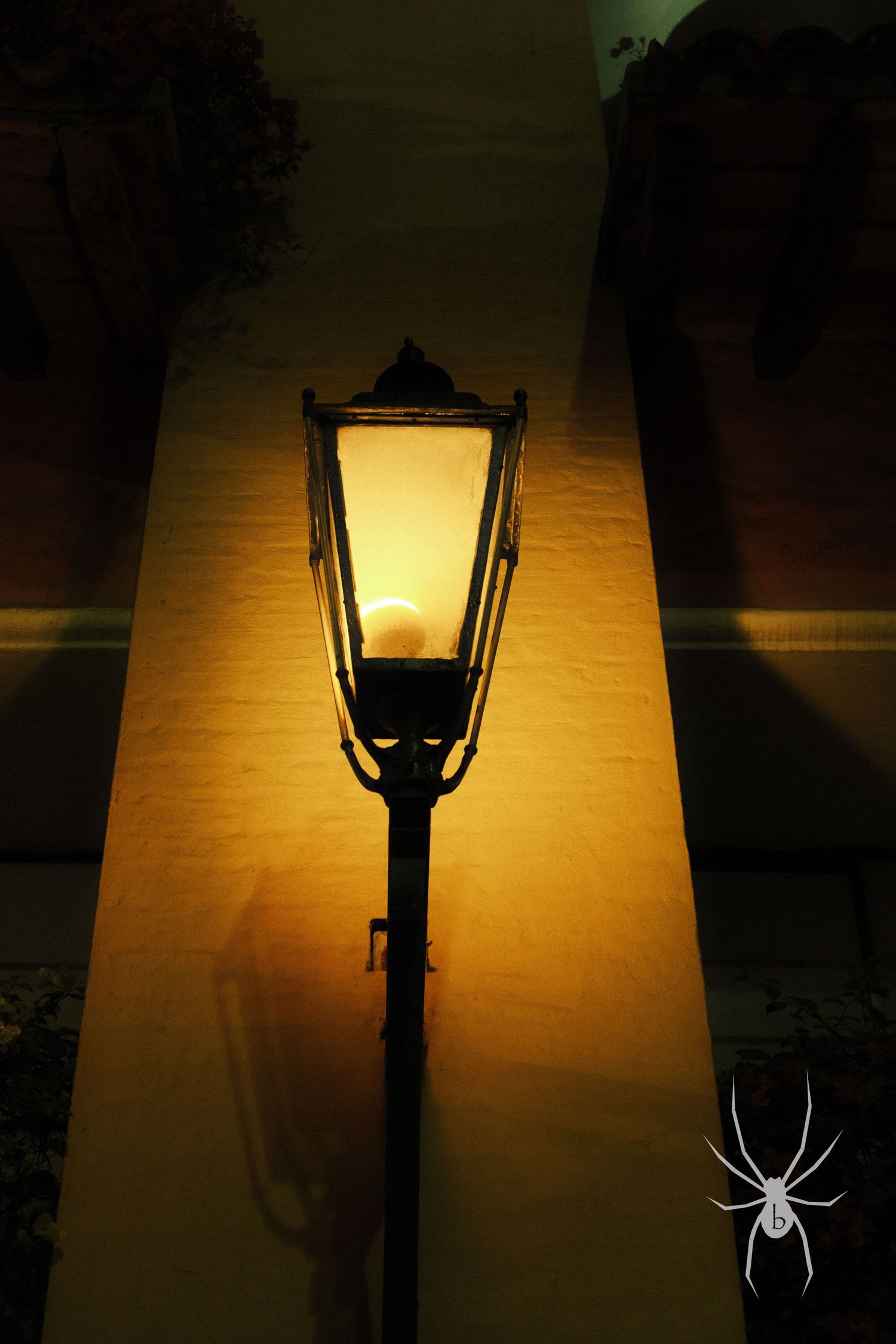 Illuminated vintage street lamp glowing in warm light against dark background with spider motif.