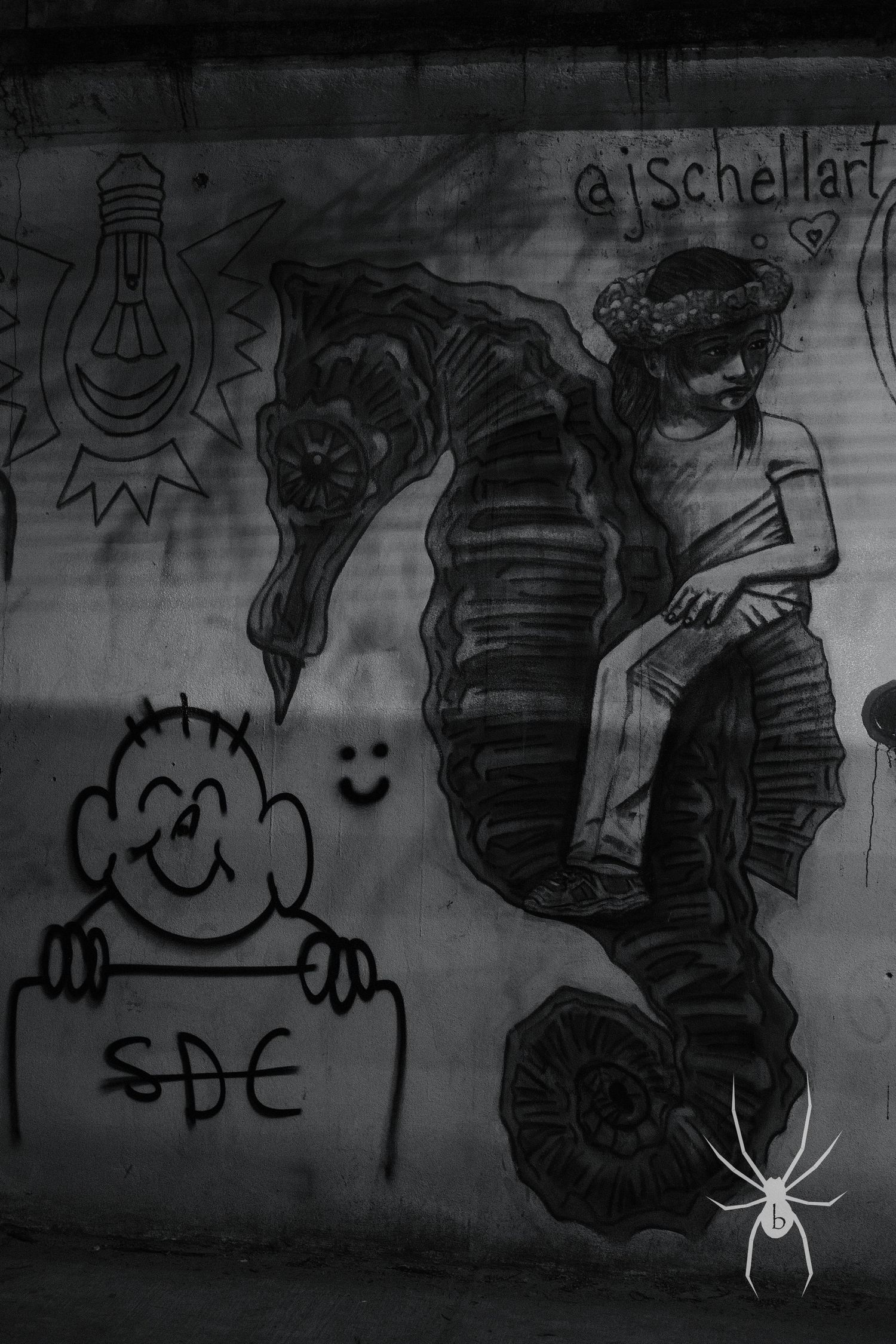 Black and white graffiti art featuring a seahorse and smiling figure on a wall.