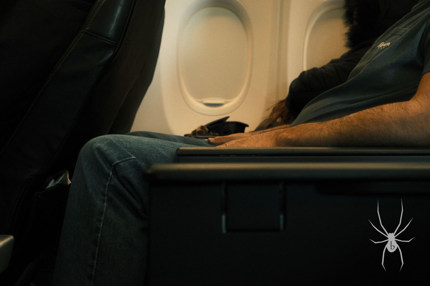 Close-up view of airplane window and passenger seat showing denim-clad leg.