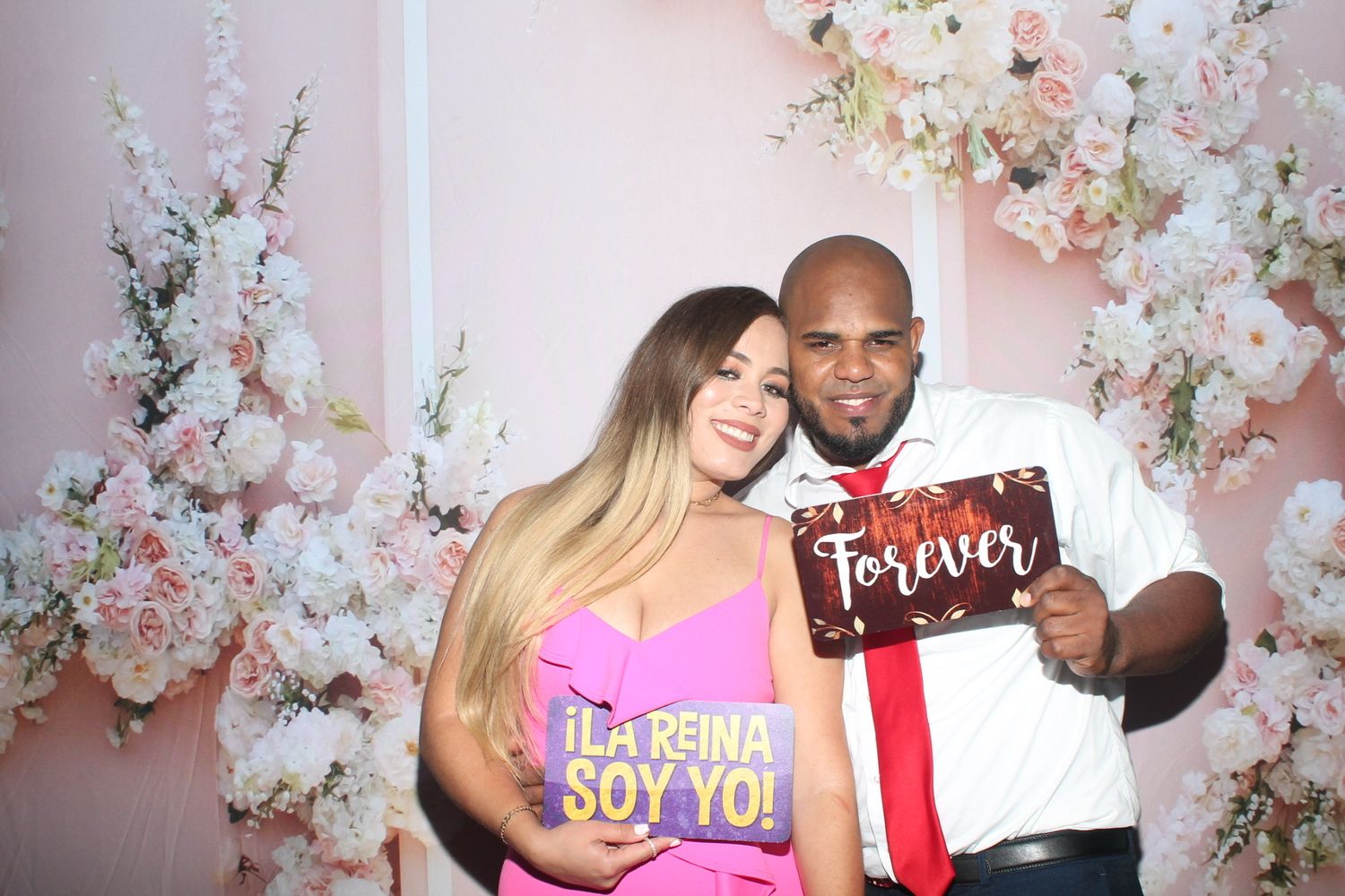 Couple posing with photo props against floral backdrop in photo booth setting.