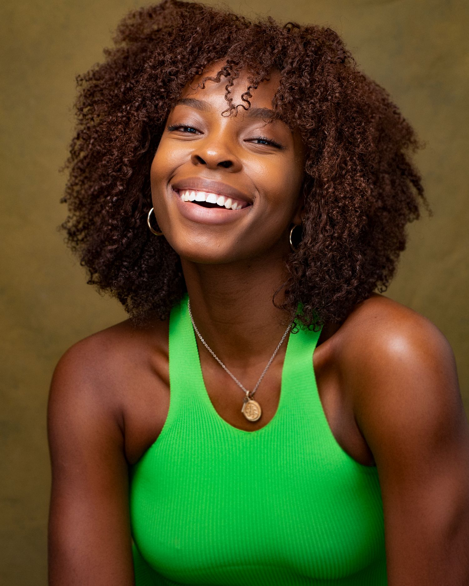 Studio portrait featuring a bright green tank top and natural curly hair against golden background.
