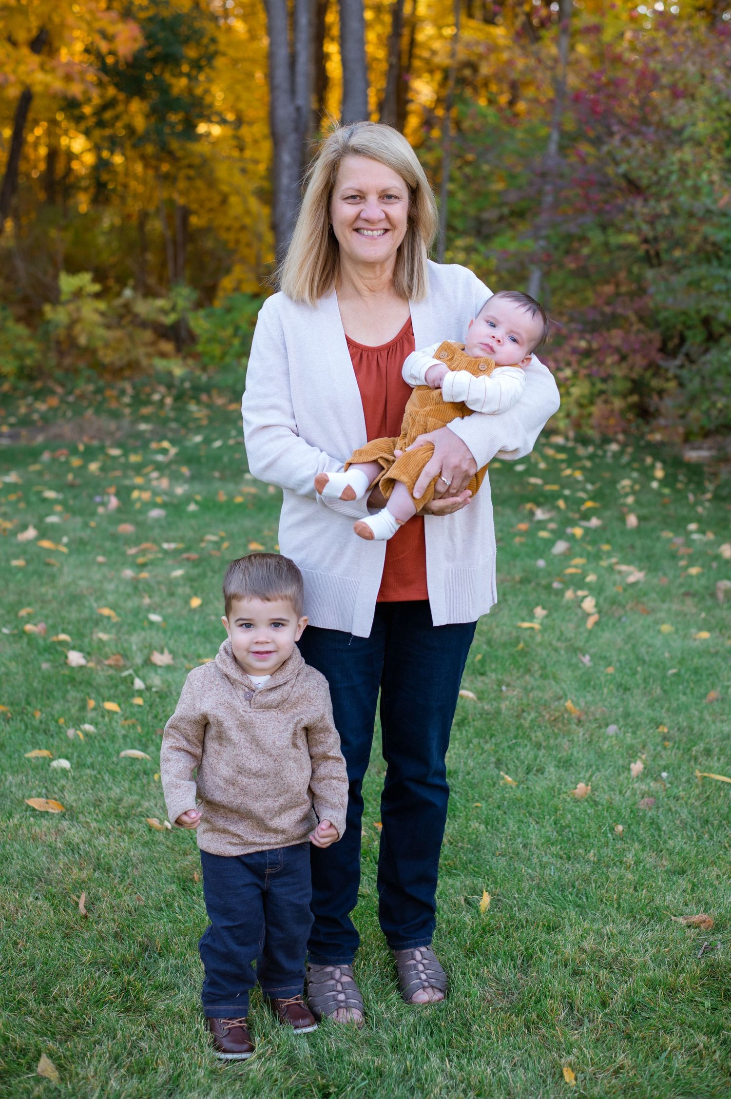 A woman and two children pose for a portrait on grass with autumn trees in the background.