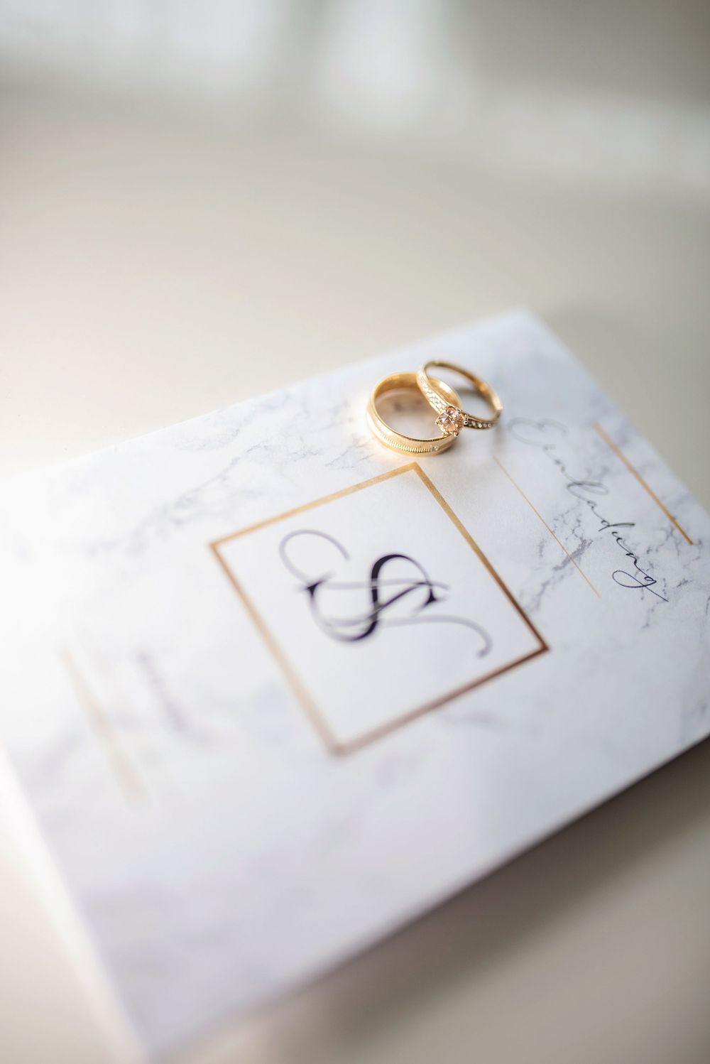 Wedding rings placed on white invitation card with gold monogram design.