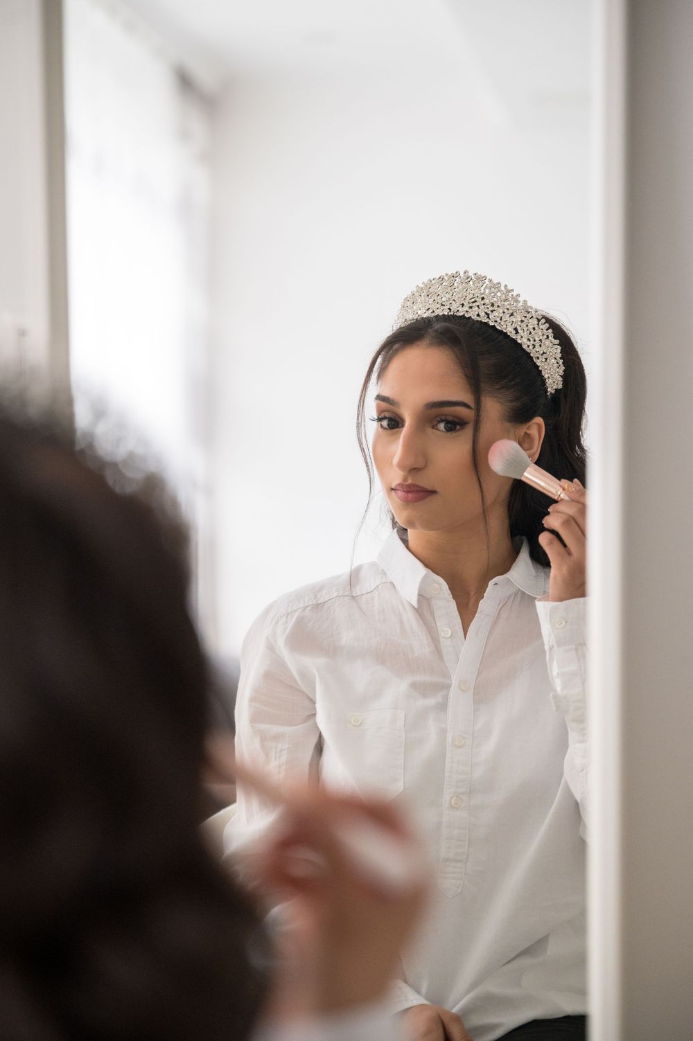 Wedding preparation scene with crystal headpiece and makeup being applied in bright room.