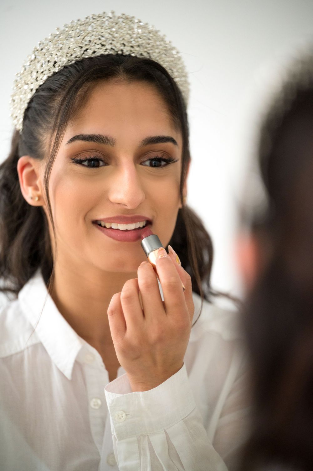 Bridal makeup session showing application of lipstick while wearing crystal headpiece.