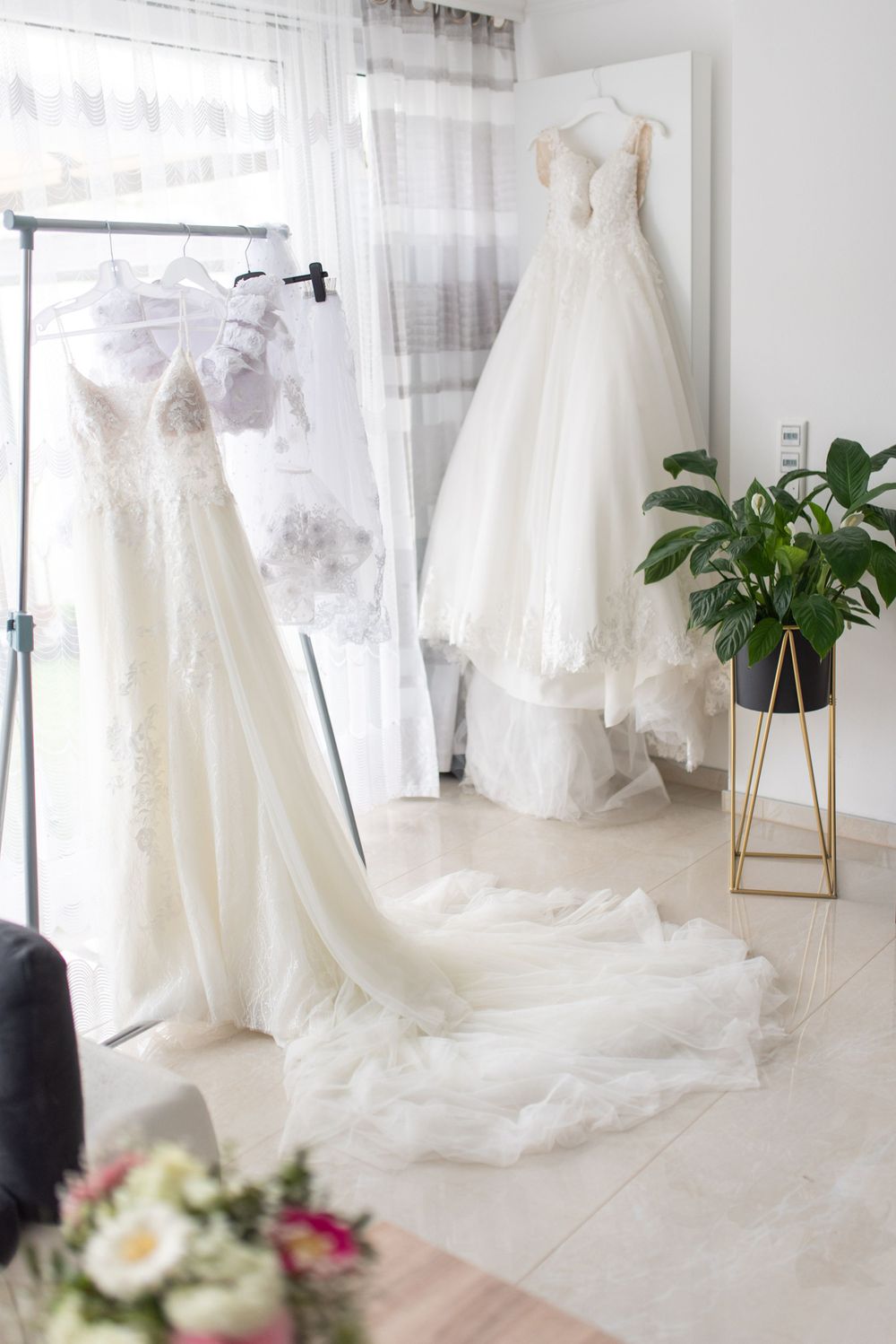 Wedding dress display in bright room with hanging gowns and decorative plant stand.