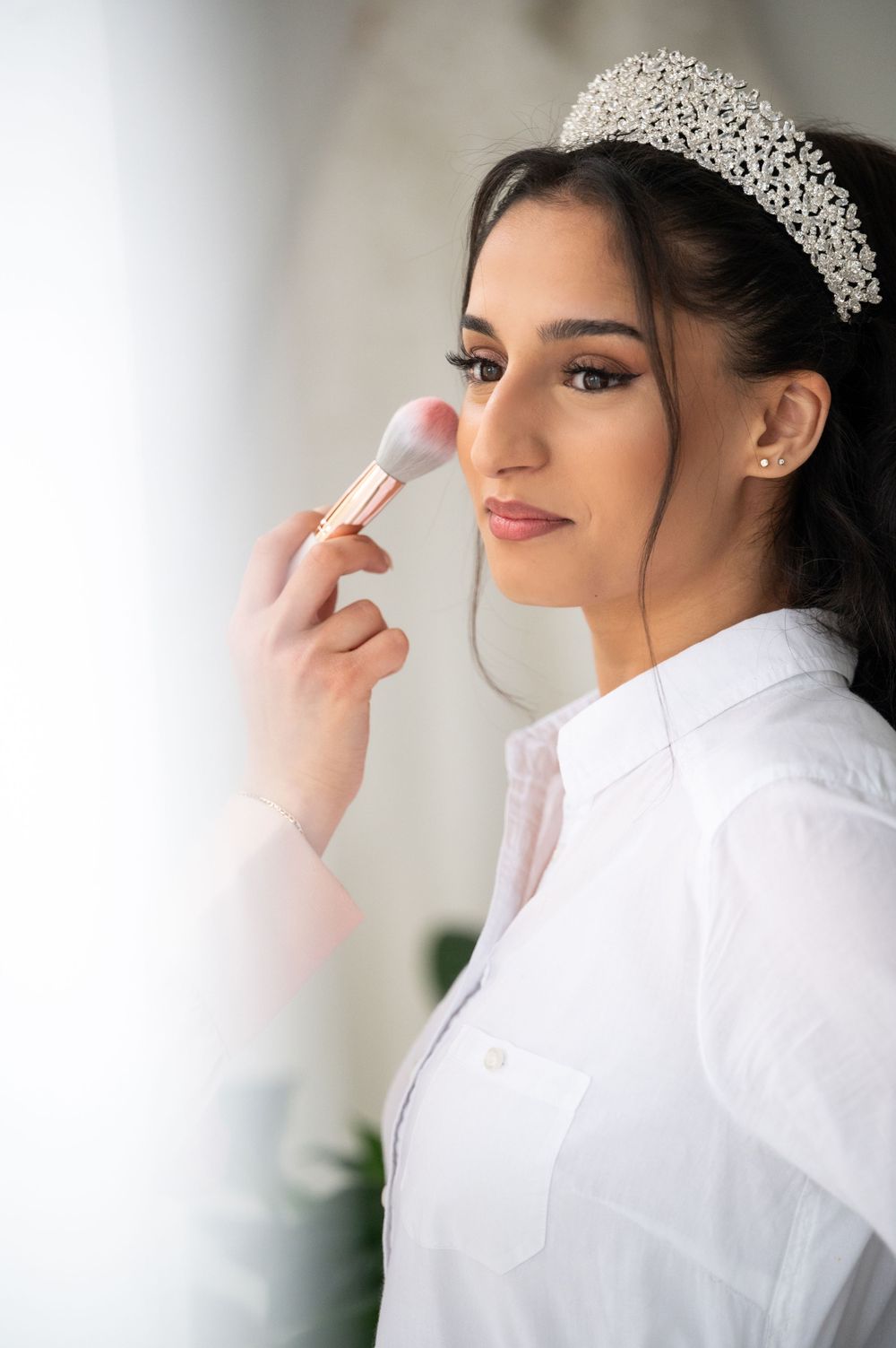 Makeup artist applying cosmetics during bridal preparation with ornate crystal headpiece.