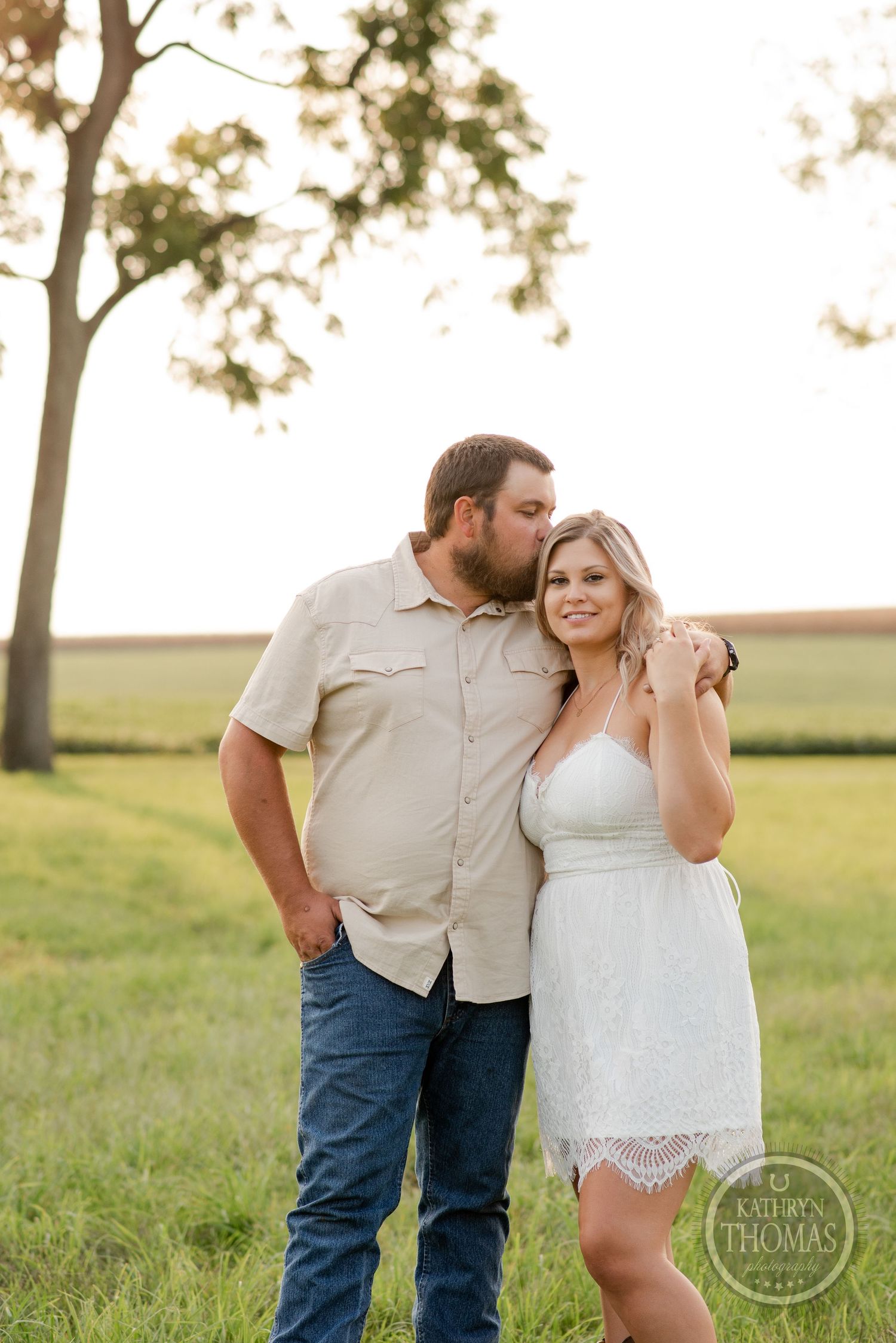 A tender moment captured between a couple in casual country attire against a rural backdrop.