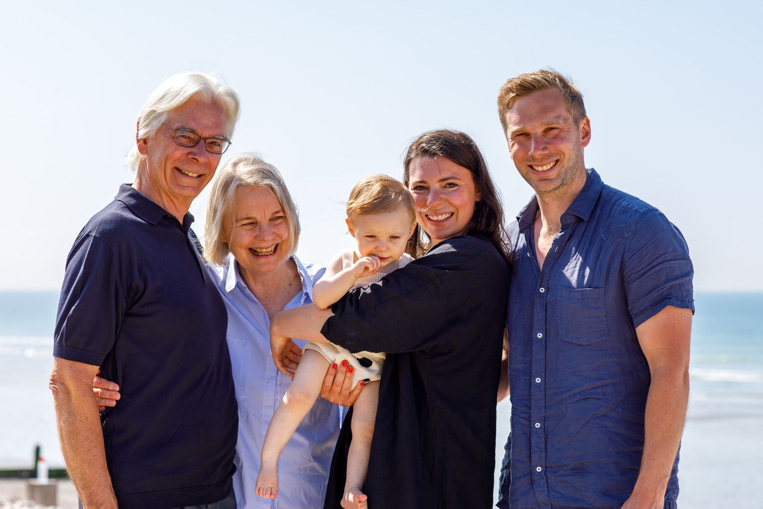 Multi-generational family gathering for a portrait on a sunny beach day.