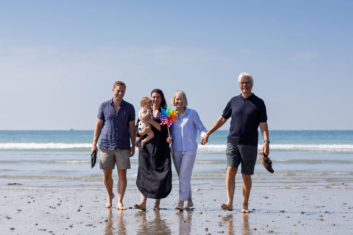 Family walking together along the shoreline on a bright beach day.