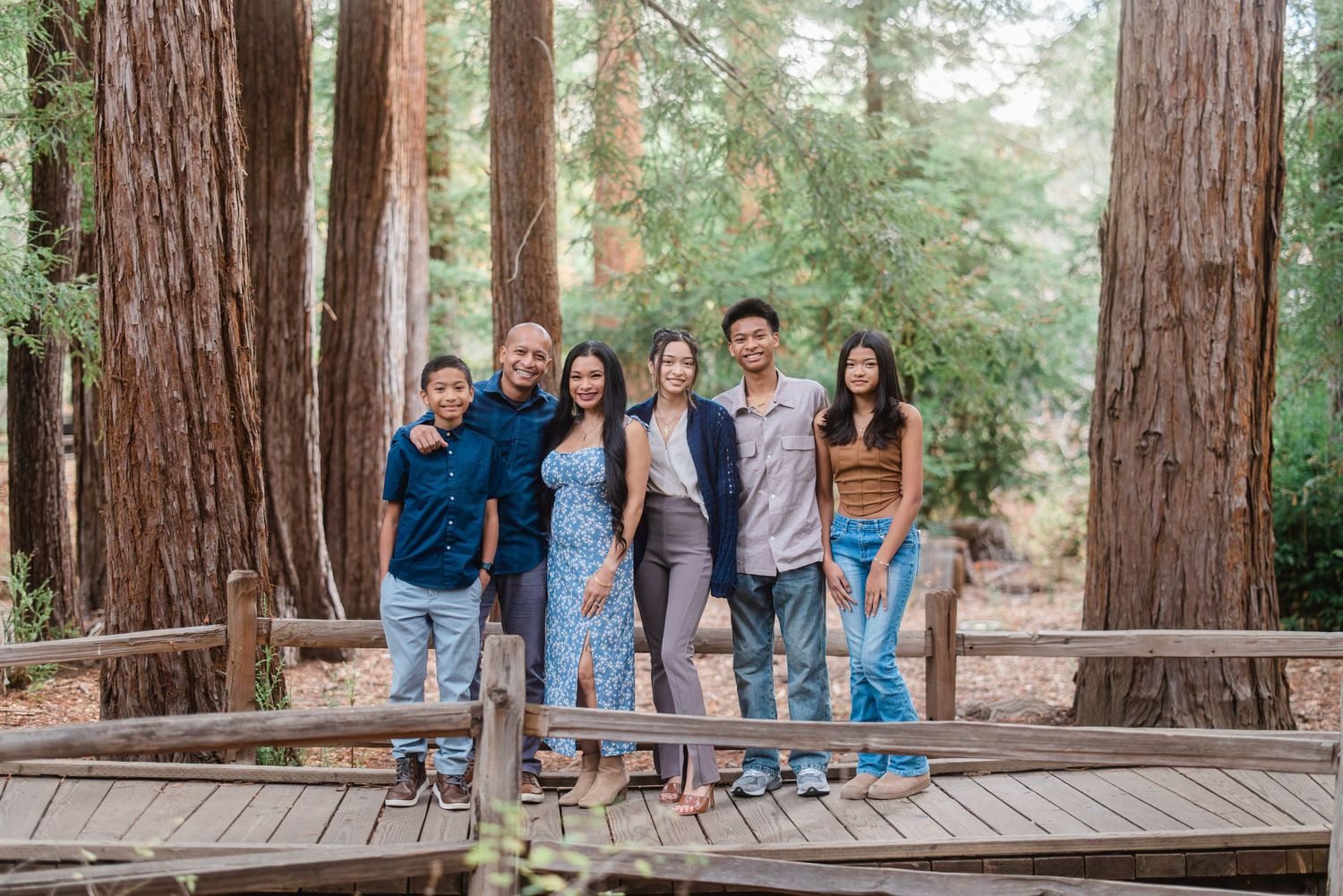 Seven people pose together on a wooden bridge in a redwood forest setting.