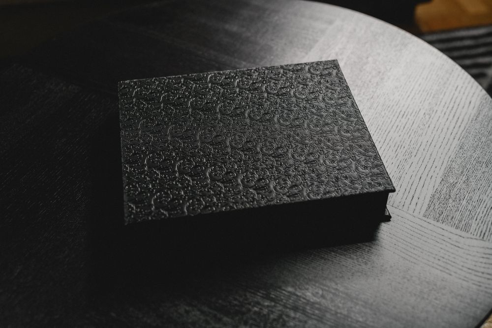 A black textured box with intricate pattern detail sits on a dark surface.