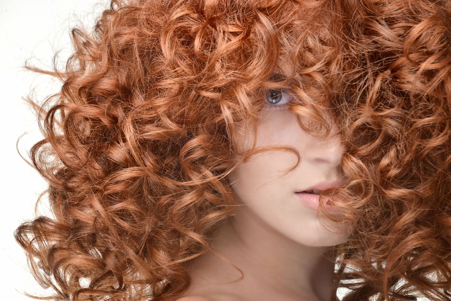 Beauty portrait showcasing natural red curly hair covering part of face against white background.