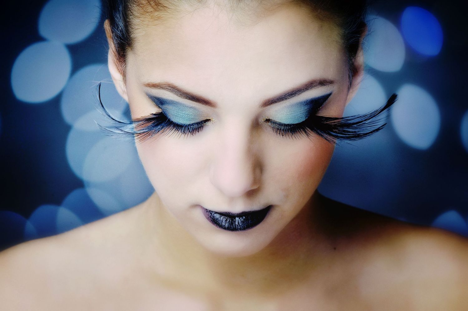 Dramatic makeup with long false eyelashes and blue eyeshadow against bokeh background.