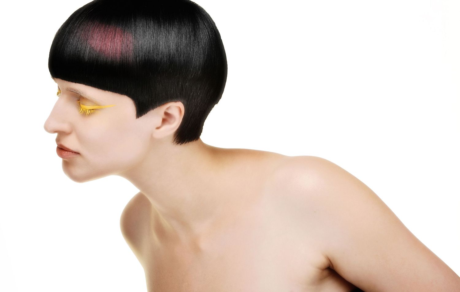 Artistic profile portrait with short black hair and gold accent makeup against dark background.
