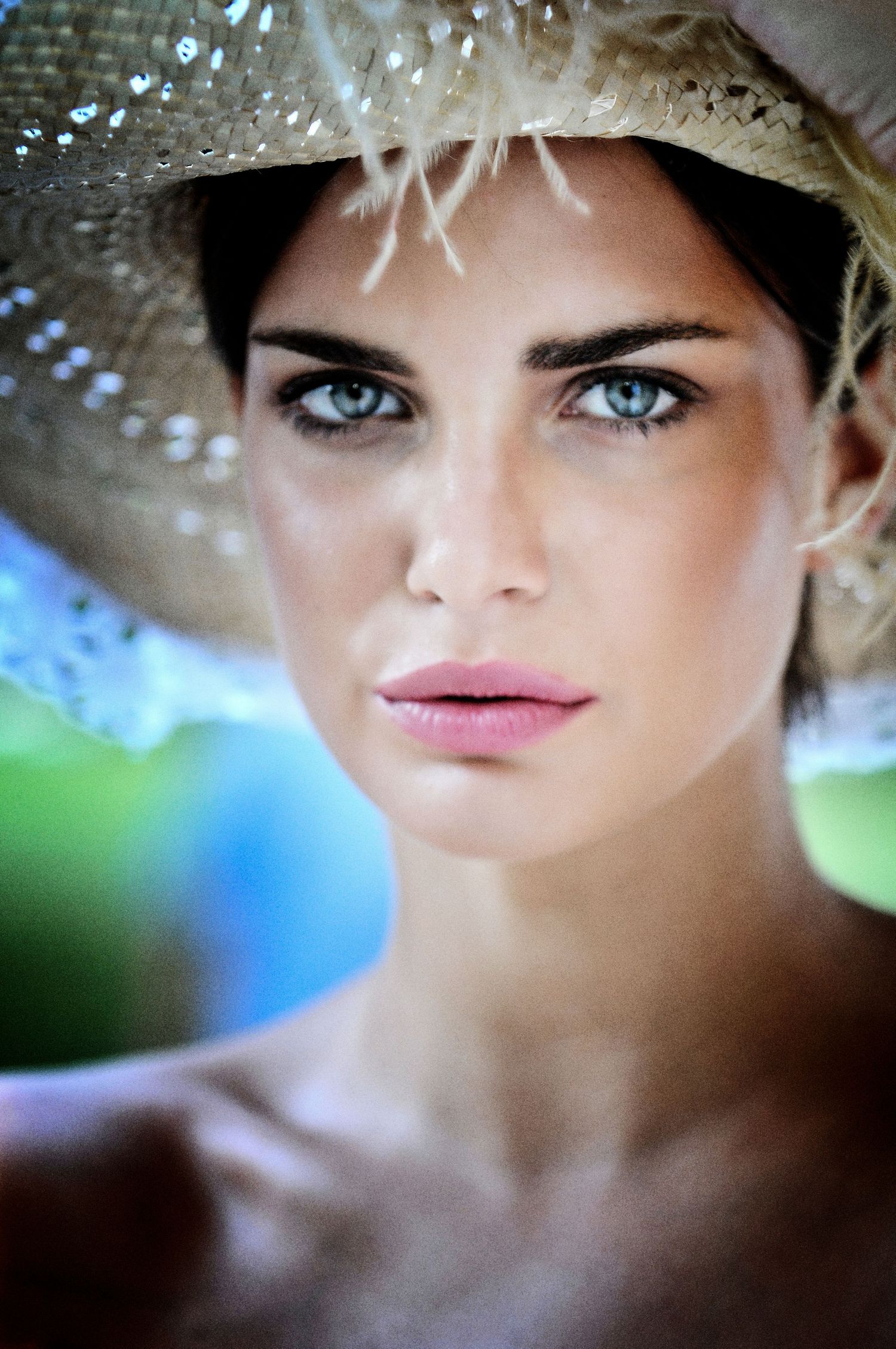 Close-up beauty portrait with straw hat and striking blue eyes in soft lighting.